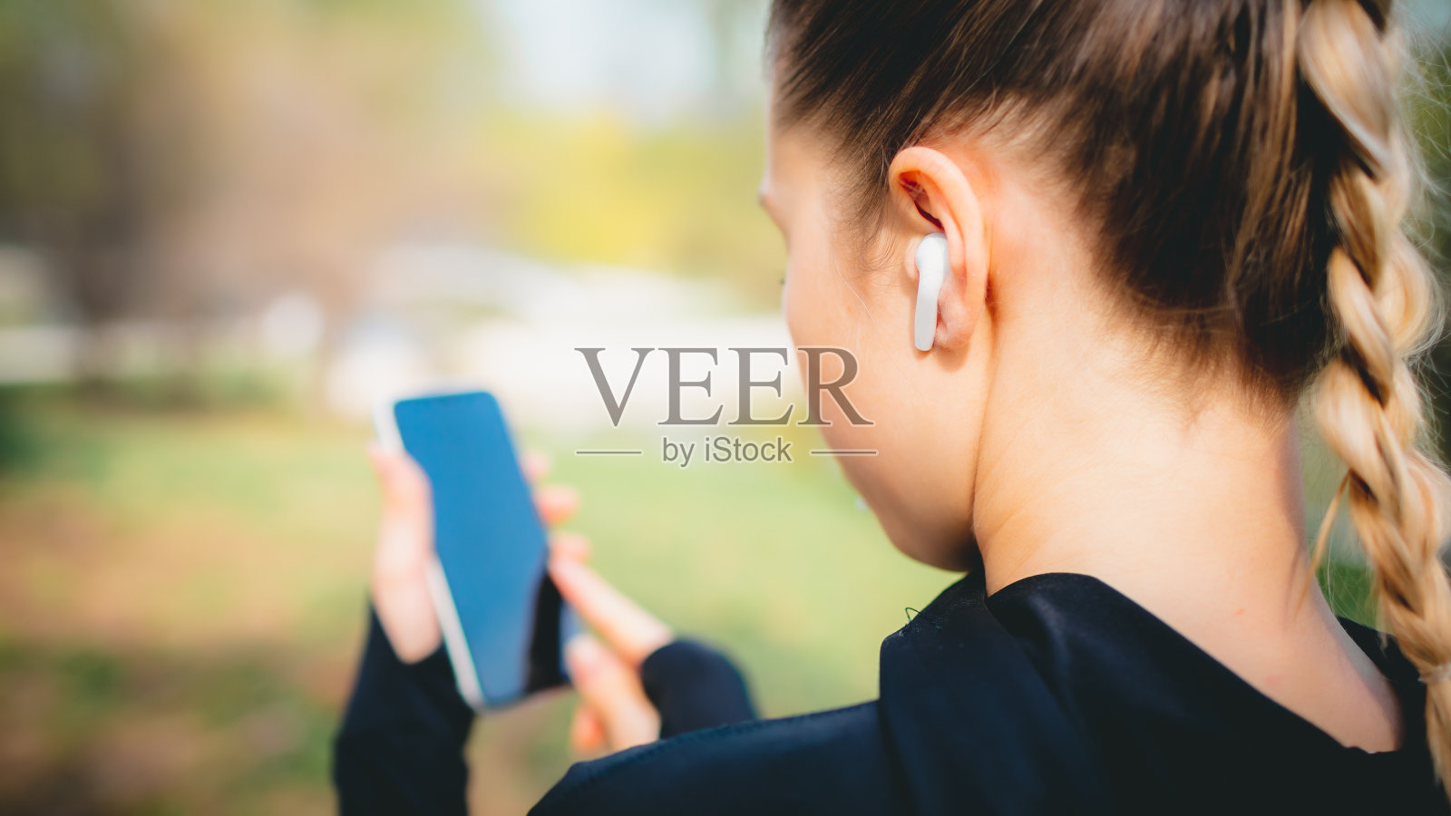 小女孩用手机和无线耳机在公园里做运动照片摄影图片