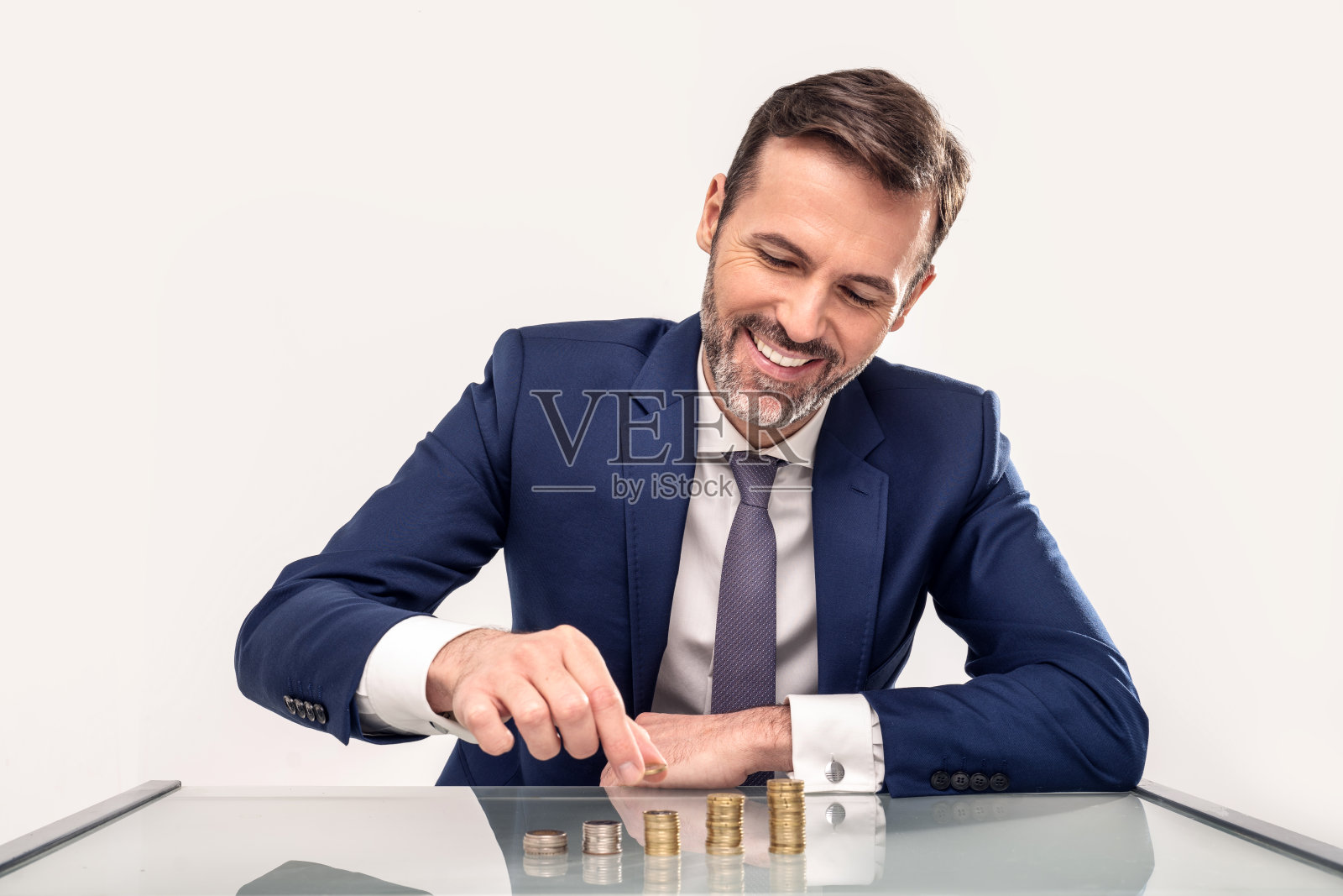 微笑的英俊商人把硬币堆在硬币堆上。概念上的照片。影棚拍摄。照片摄影图片