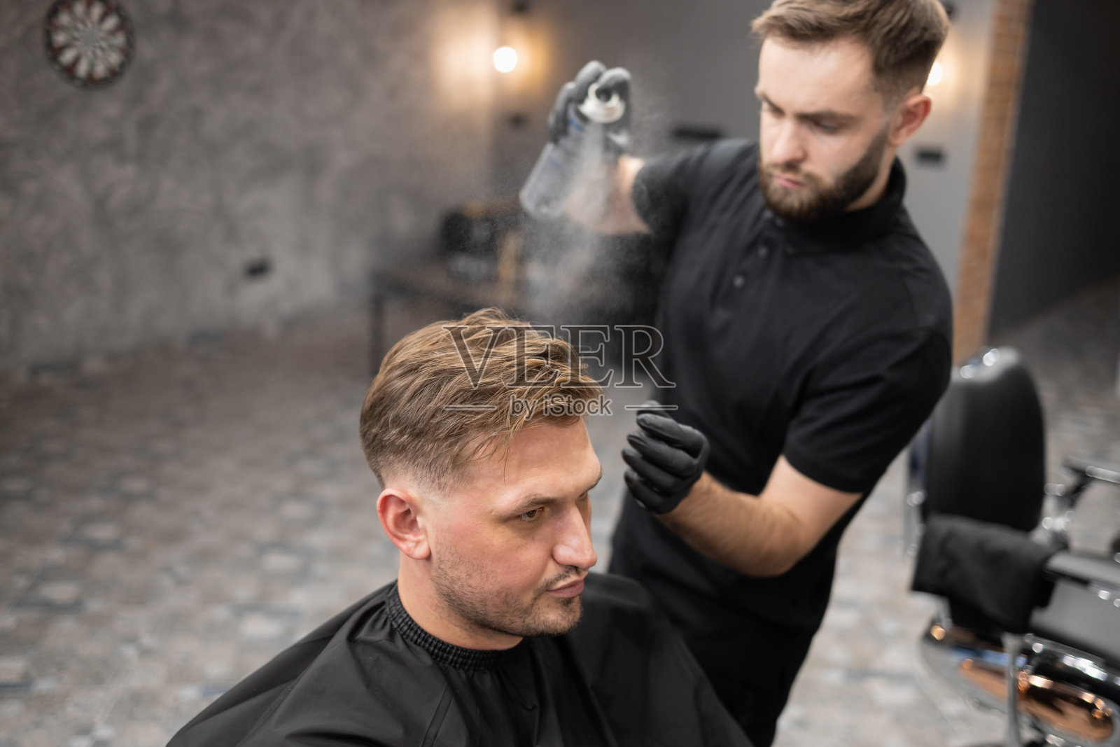 理发师在理发店里给坐在椅子上的男顾客涂发胶理发师给一个男人理发照片摄影图片