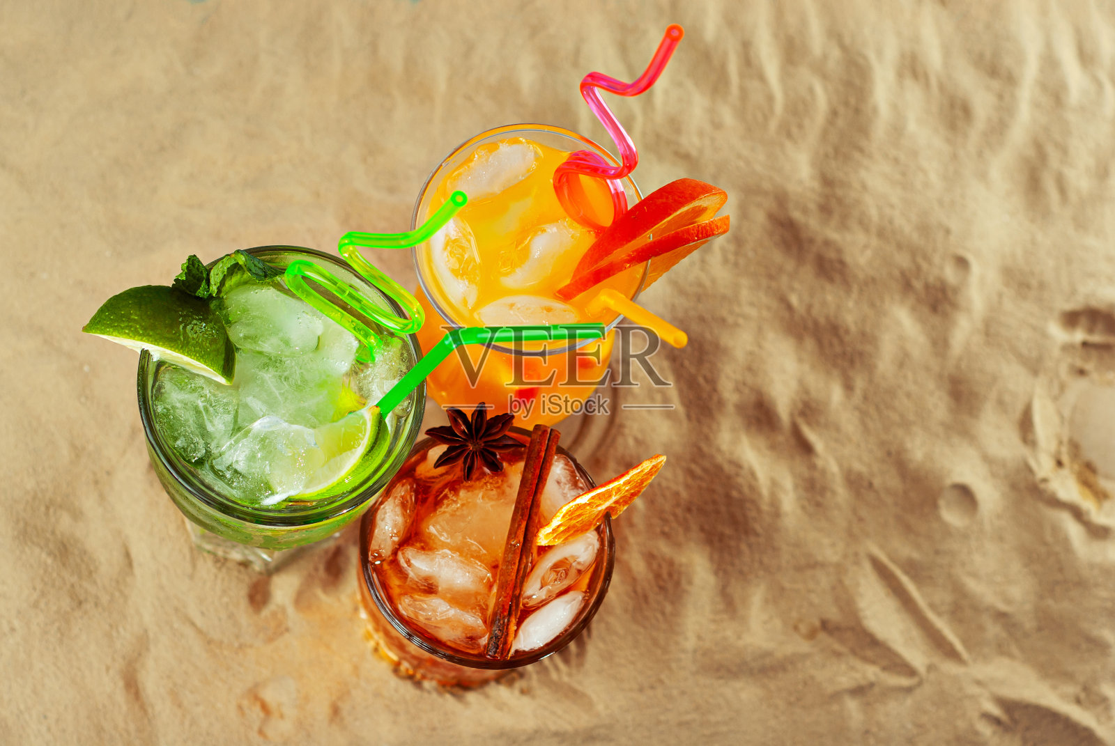 橙色和绿色的鸡尾酒在沙滩上。酒精饮料,在沙子上加冰、橘子、薄荷和石灰。照片摄影图片
