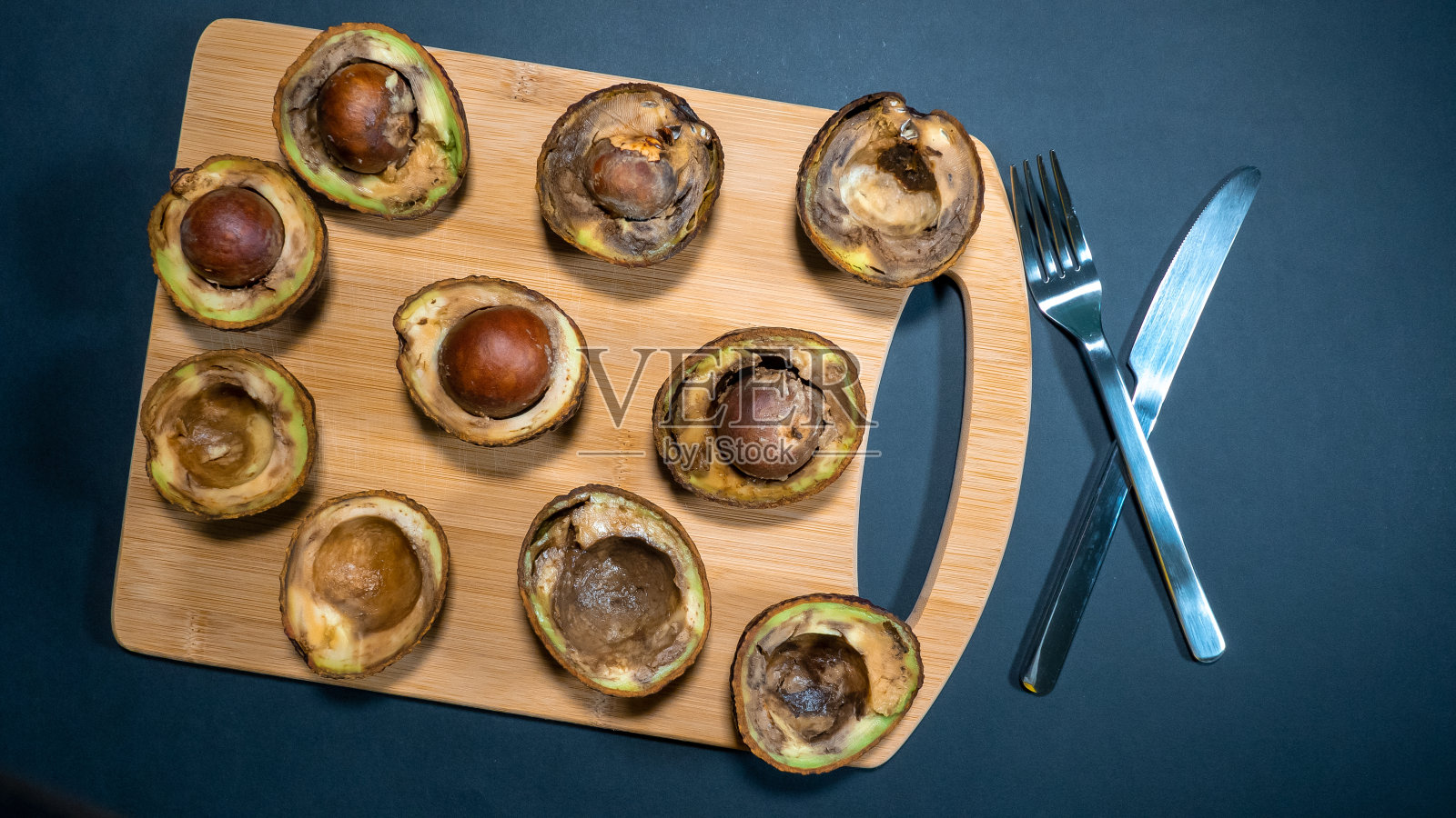 牛油果烂在木头上,切碎机下刀叉。照片摄影图片