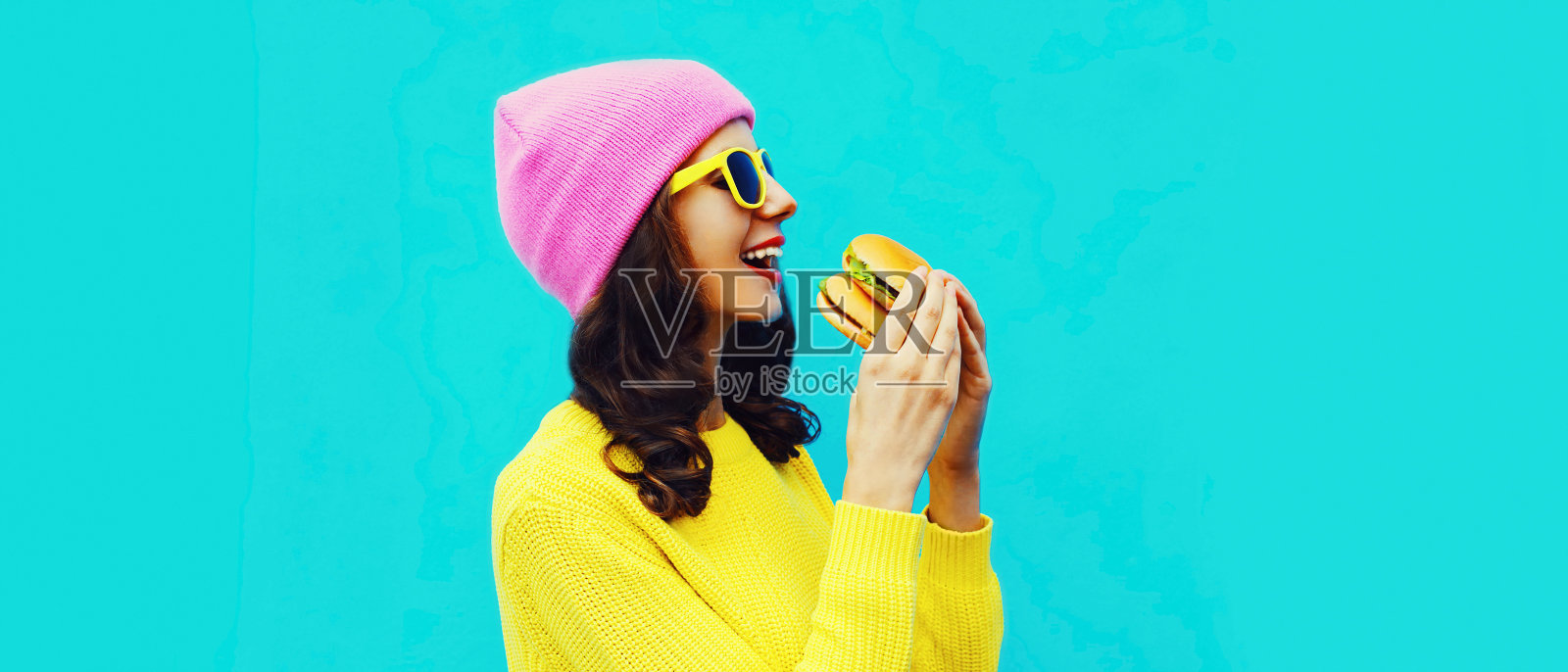 时尚的快乐微笑的年轻女子的肖像吃一个美味的大汉堡快餐在蓝色彩色背景照片摄影图片
