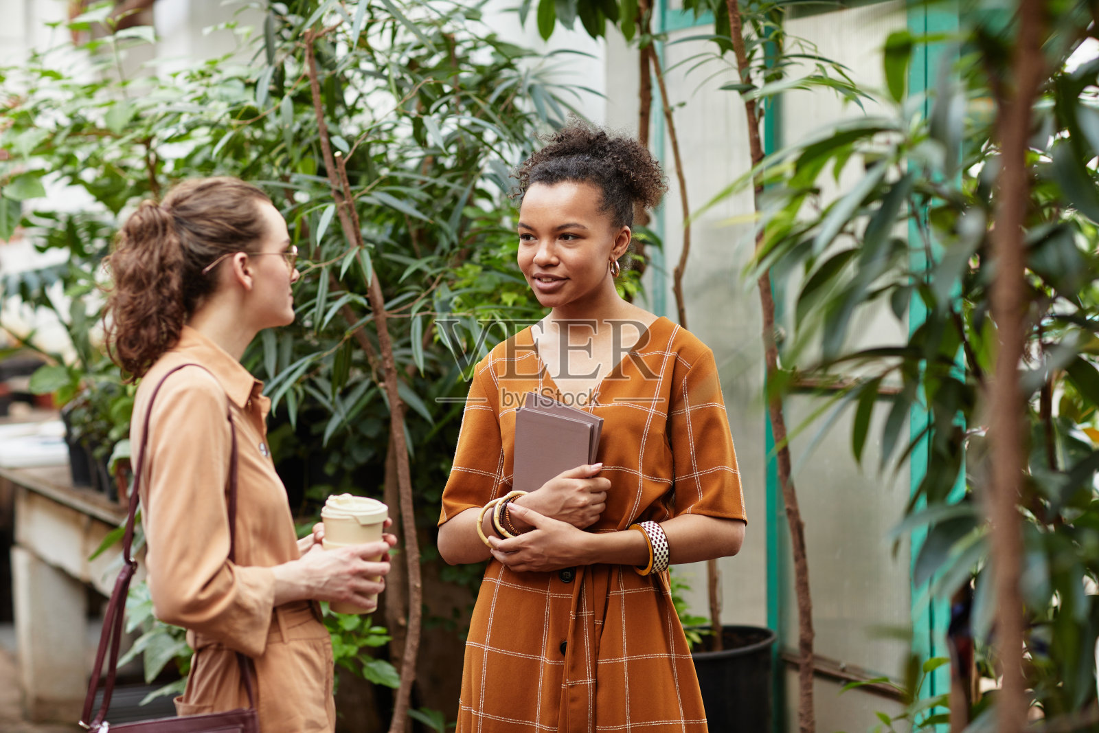 年轻优雅的女花商正拿着一杯咖啡在服装上咨询客户照片摄影图片