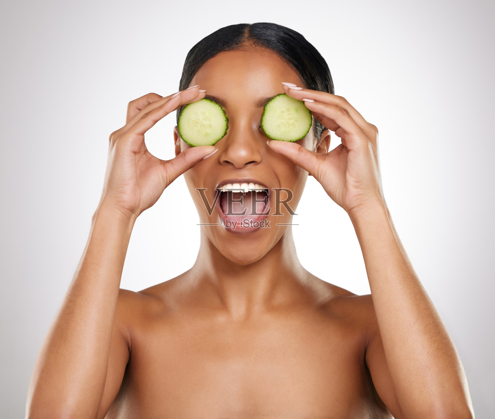 这是一名年轻迷人的女子在灰色背景下拿着两片黄瓜摆姿势的工作室照片照片摄影图片