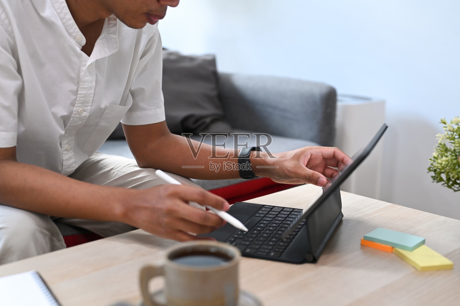 裁切拍摄的年轻商人坐在沙发上工作与电脑平板电脑。照片摄影图片