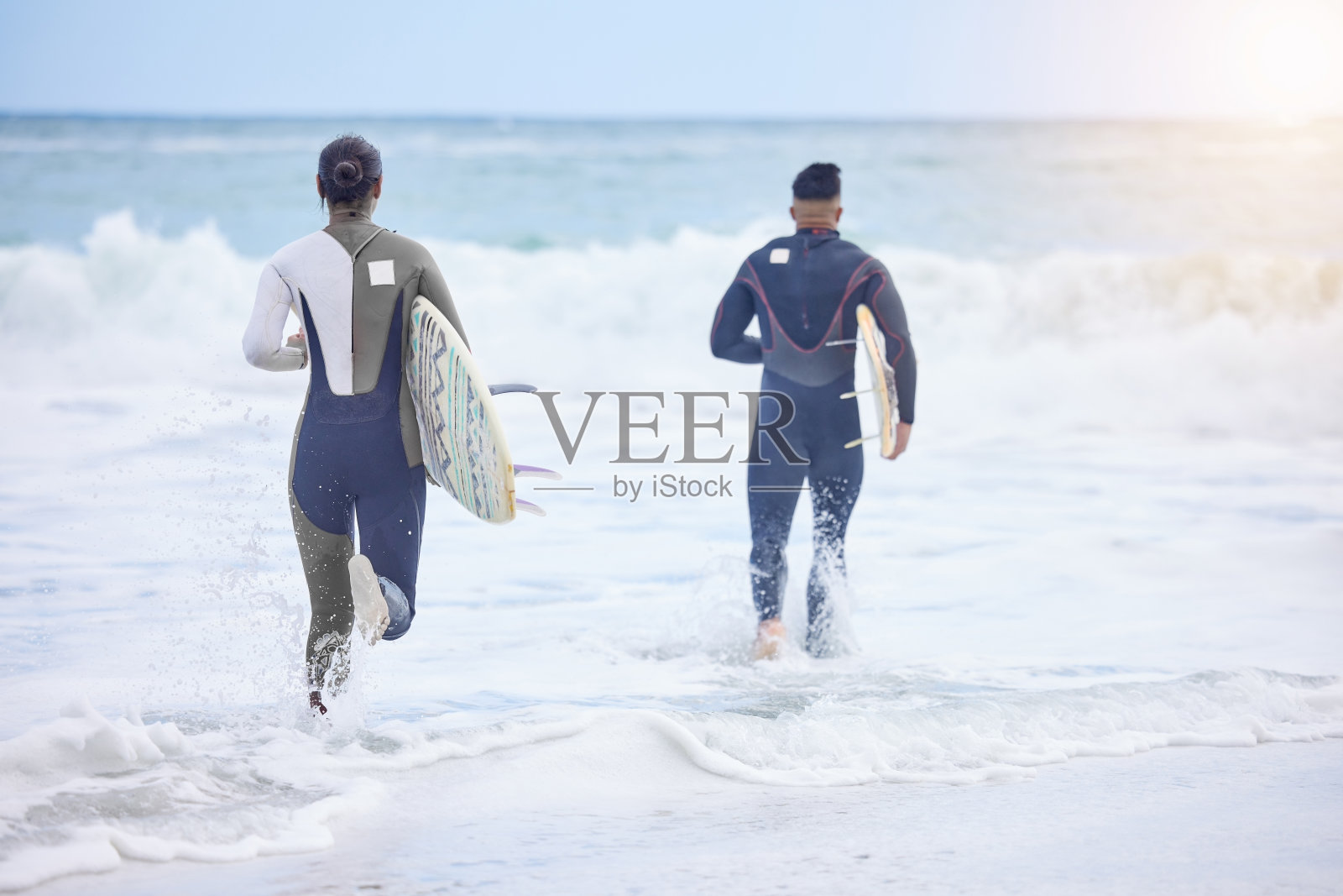 后视镜拍摄的一对年轻夫妇跑向大海与他们的冲浪板照片摄影图片