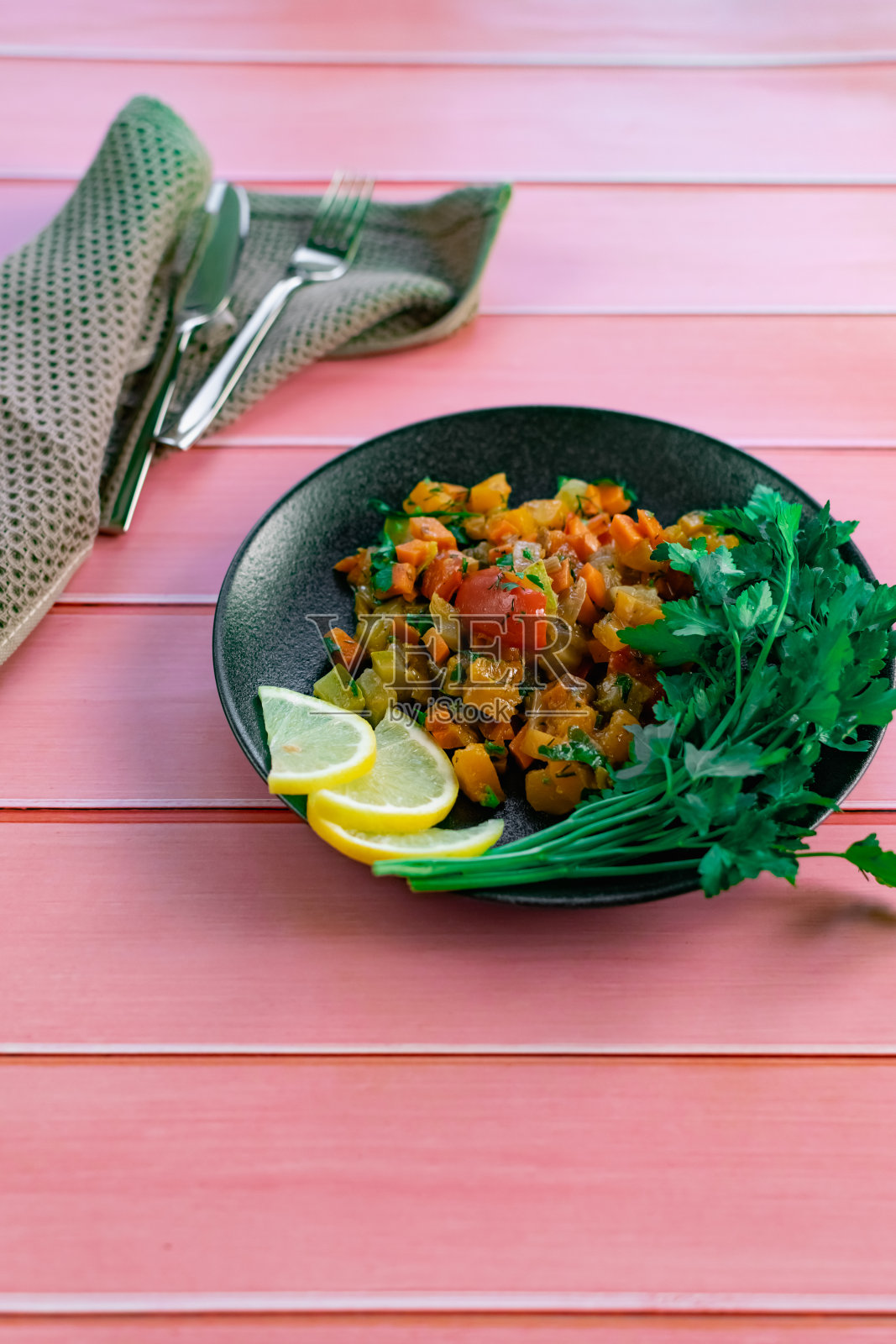 黑盘子里的法式蔬菜杂烩,用新鲜的欧芹叶和柠檬片着色,粉红色的木制背景,许多国家都能负担得起的一道菜照片摄影图片