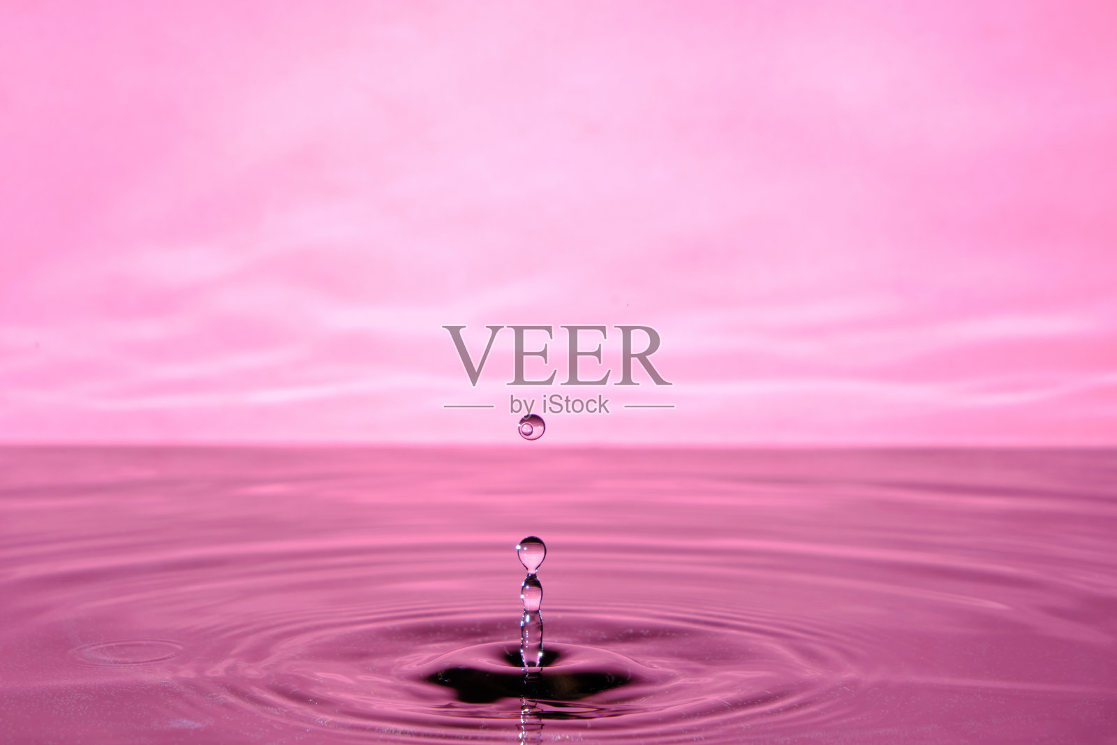 滴水后溅起水花。粉红色抽象背景与水滴在水。照片摄影图片