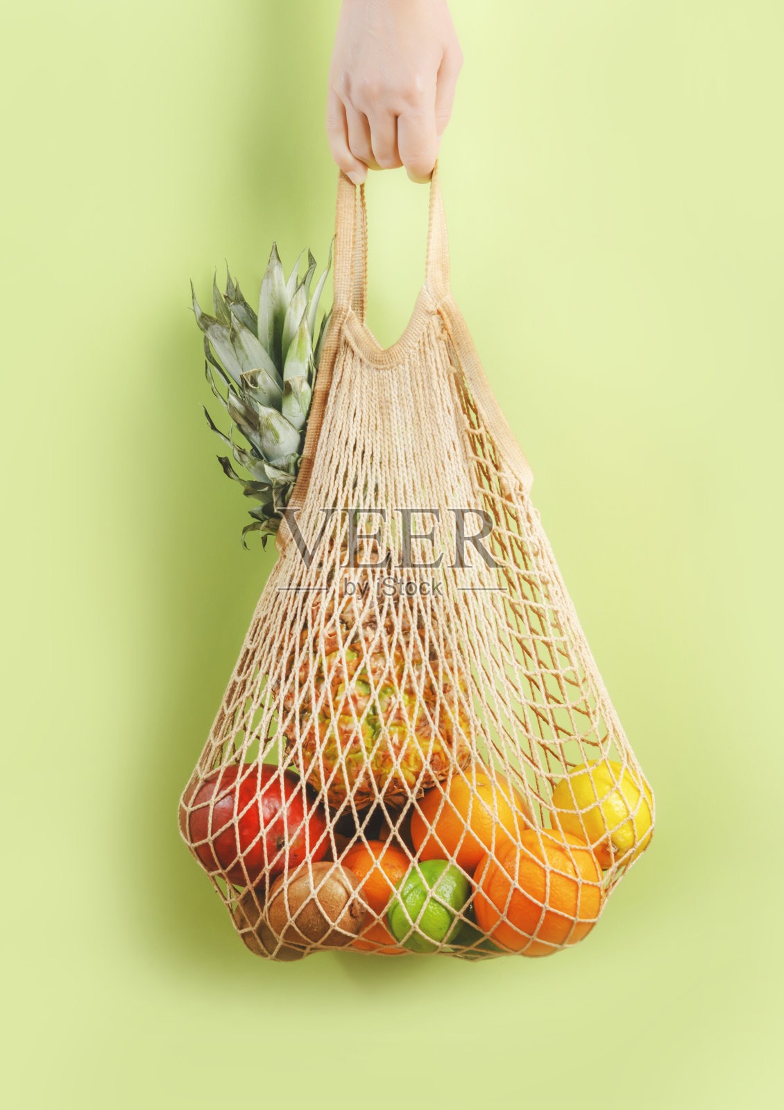 妇女手握环保购物袋与各种热带水果在绿色的背景。可持续的生活方式。塑料是免费的。“零浪费”的概念照片摄影图片