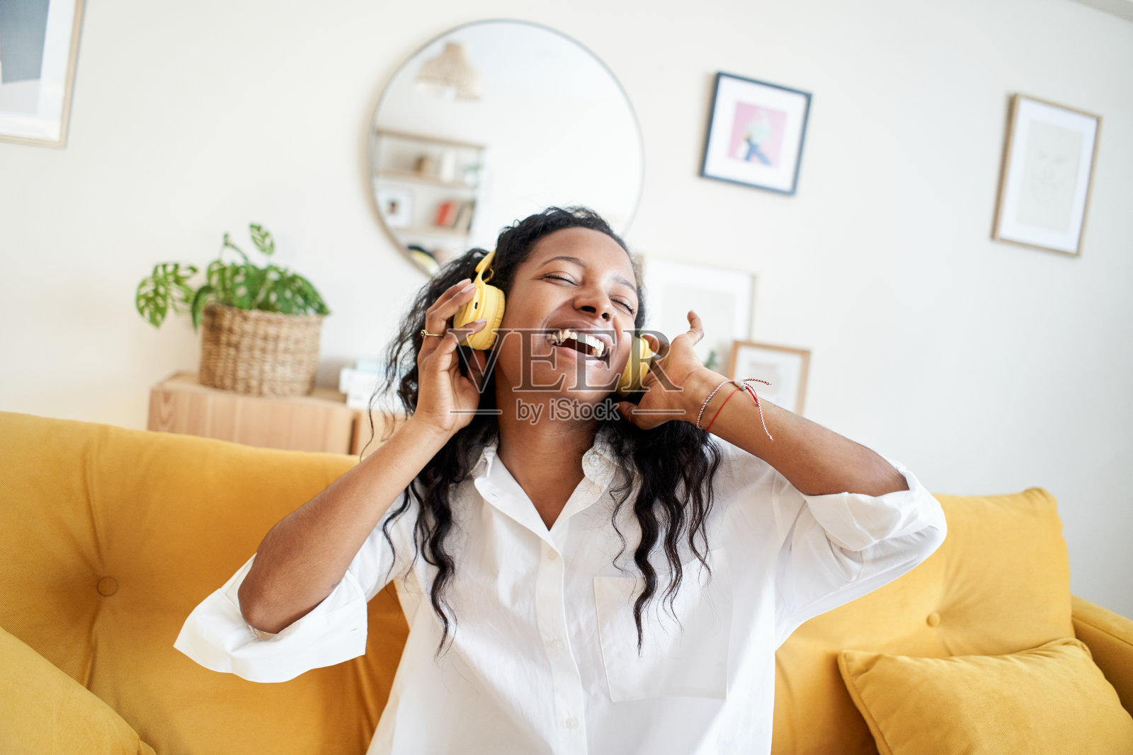 愉快的年轻女子听音乐,戴着耳机,在家里柔软的沙发上跳舞。照片摄影图片