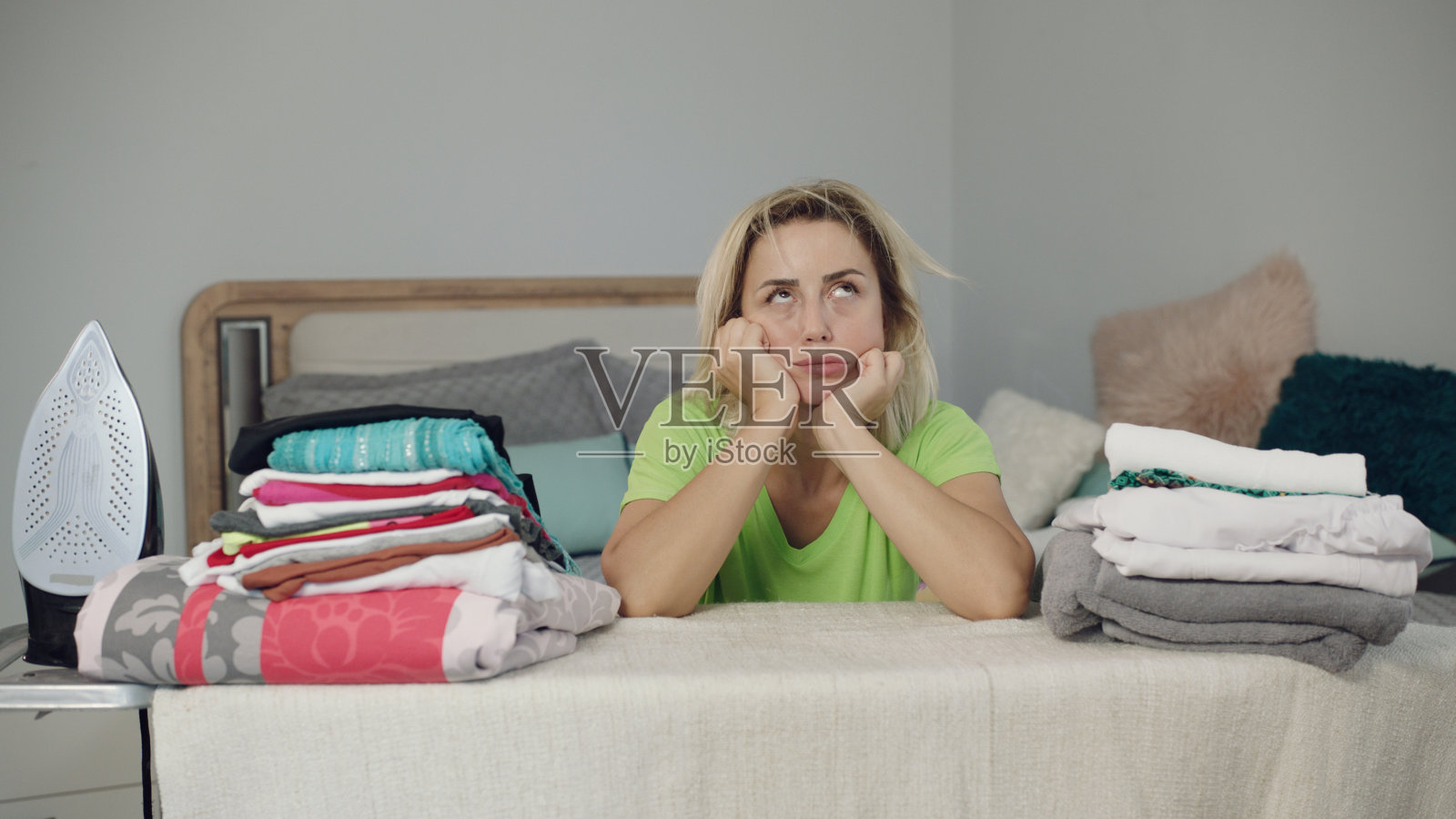 年轻女子厌倦了熨衣服,看着面前堆积如山的衣服照片摄影图片