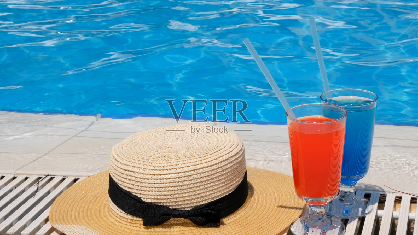两个粉红色和蓝色的彩色鸡尾酒杯,泳池边的太阳帽,近看。度假理念,酒店休闲,包罗万象照片摄影图片