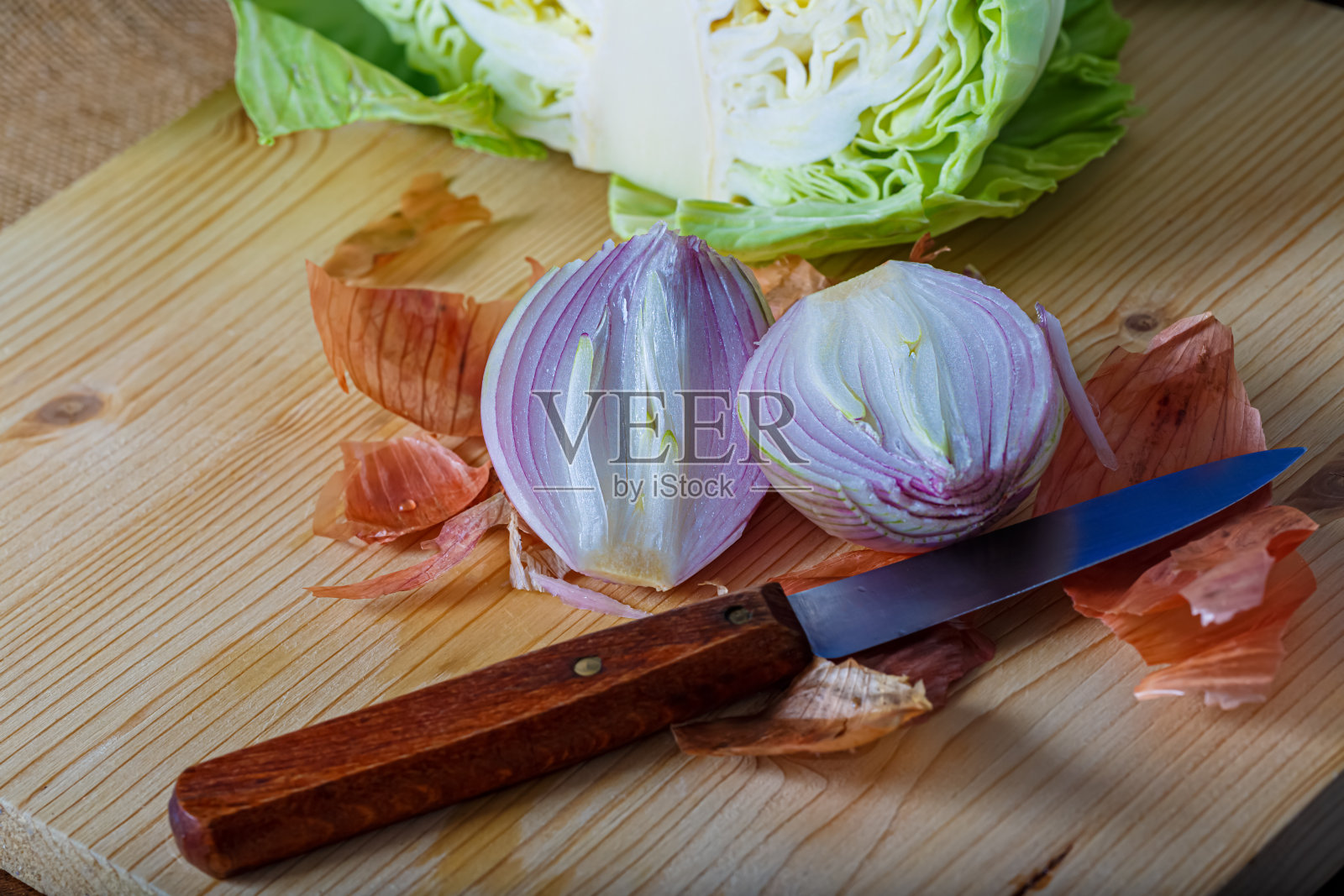 将生蔬菜切成两部分的俯视图。紫洋葱带皮和白卷心菜放在木板上,一把小刀照片摄影图片