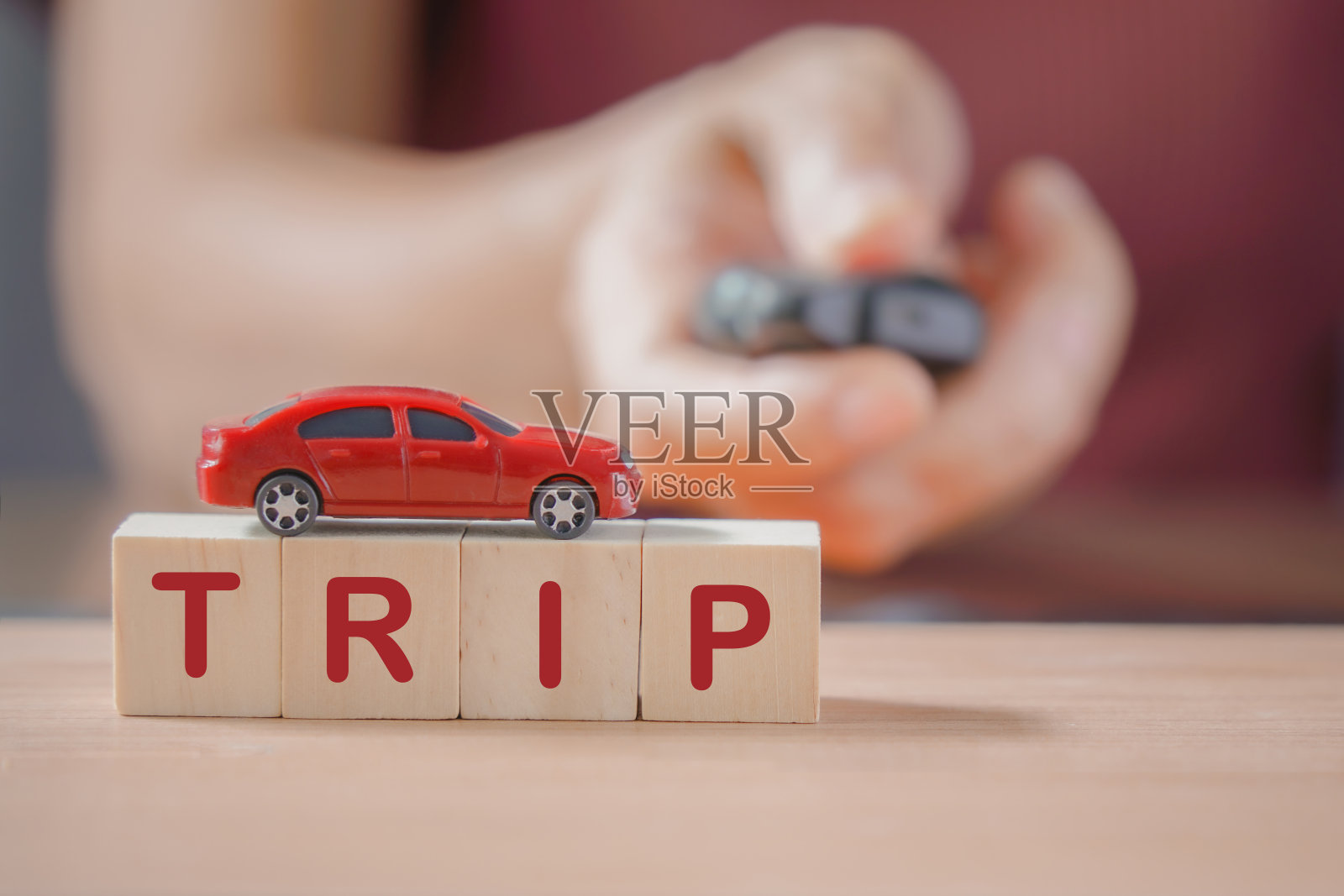 红色迷你车在木制的立方体上,带有旅行字,带有模糊的人拿着遥控钥匙,用于旅行、旅游、度假的概念照片摄影图片