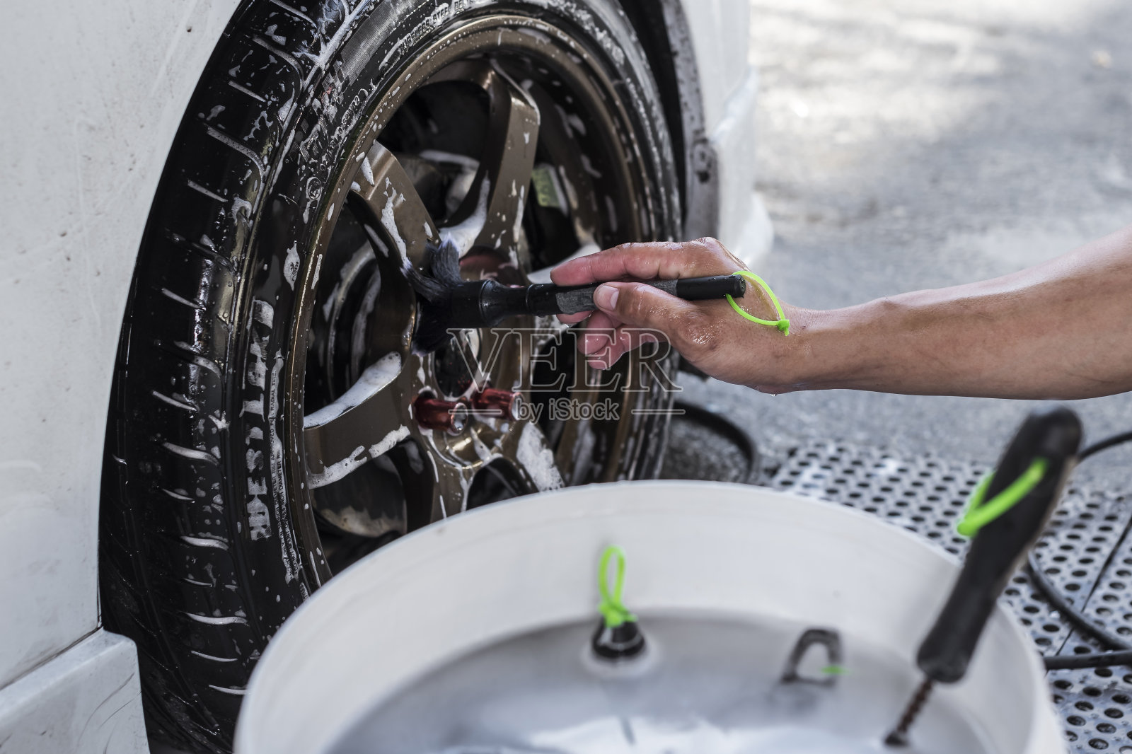 一名男子用细刷清洁汽车前轮胎边缘的凸耳螺母和中心盖。在洗车店或汽车修理店。照片摄影图片