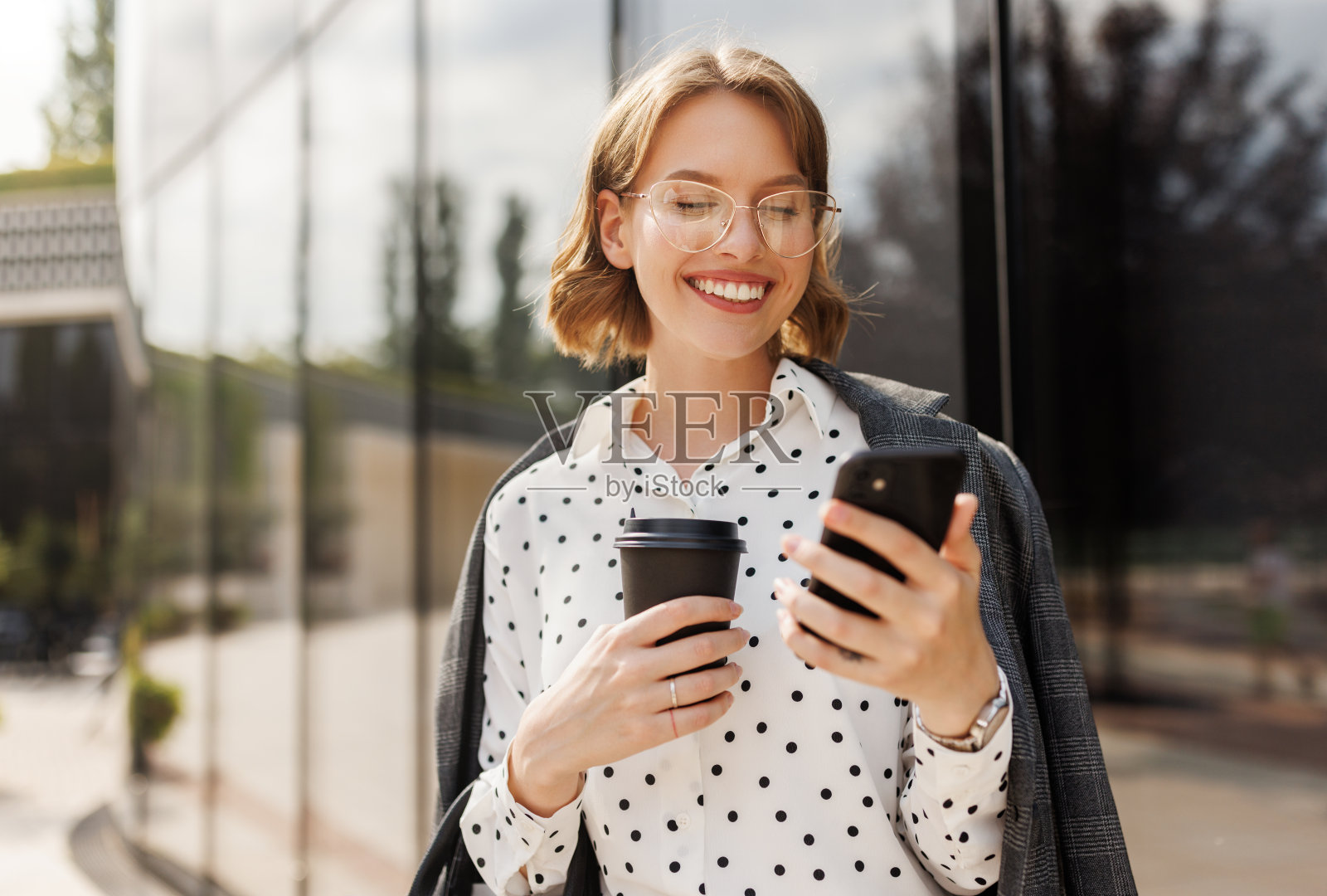 积极的商业妇女与带走咖啡使用手机,而站在阳光明媚的街道照片摄影图片