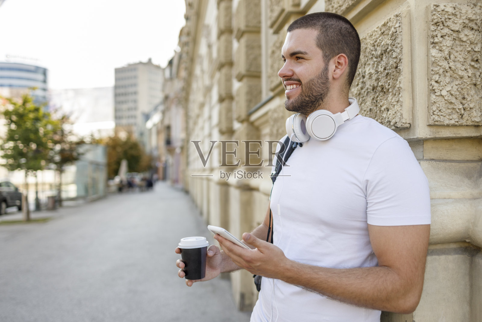 男人带着耳机,喝咖啡去,用智能手机微笑照片摄影图片