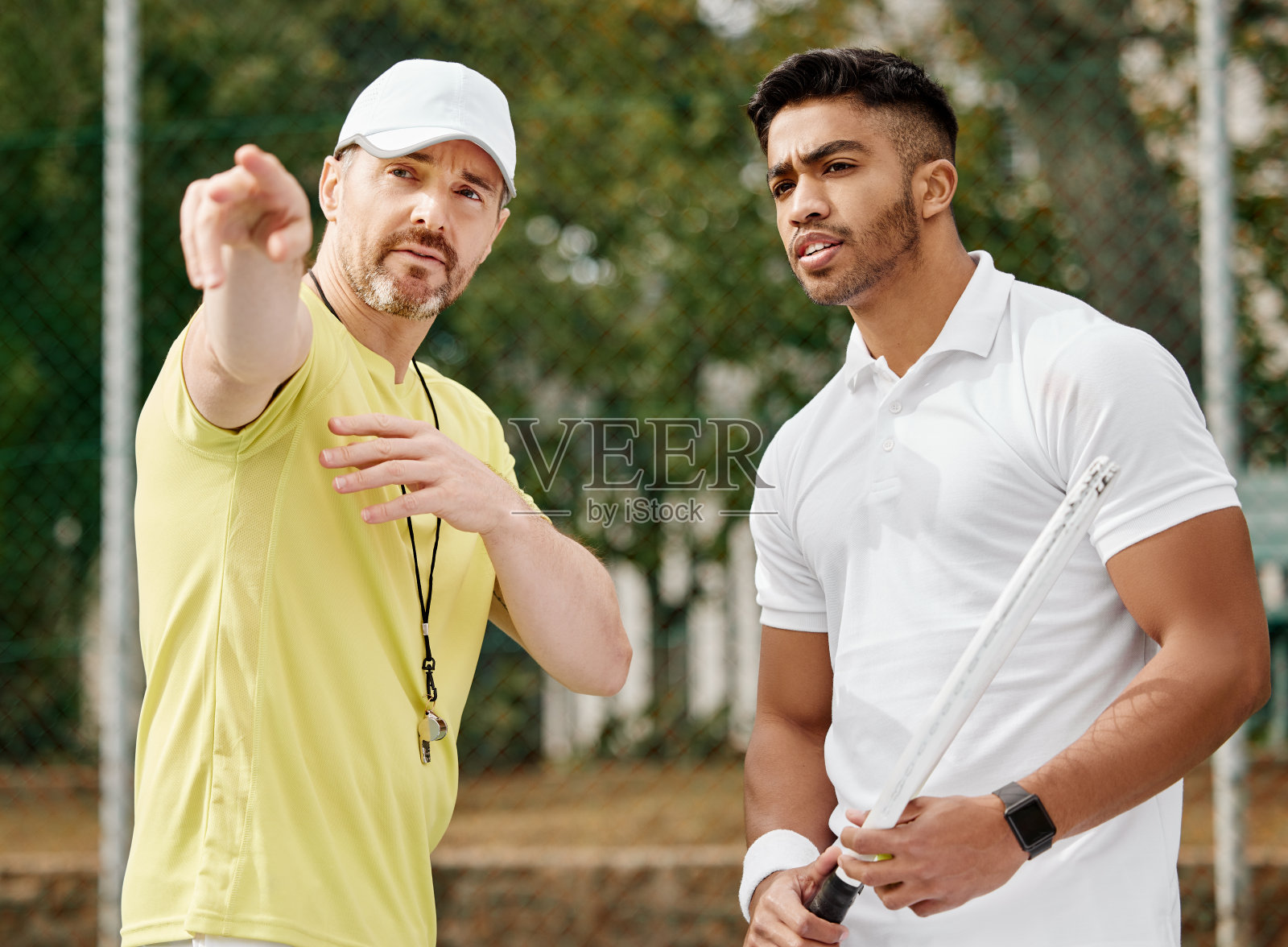 剪裁的镜头,一个英俊的男性教练给他的年轻的网球学生在一个球场上的指示照片摄影图片