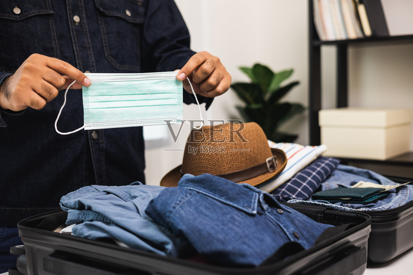 合上男性的手,用防毒面具整理行李。把衣服和裤子放在手推车里,准备出国。为暑假旅行准备行李。照片摄影图片