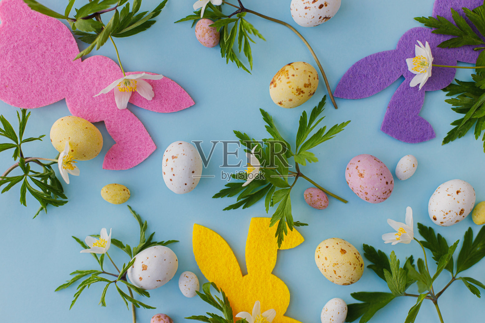 五颜六色的复活节兔子,巧克力蛋和春天的花朵平躺在蓝色的背景上。复活节快乐!粉红色和黄色的人工装饰和清新的春花。复活节狩猎照片摄影图片