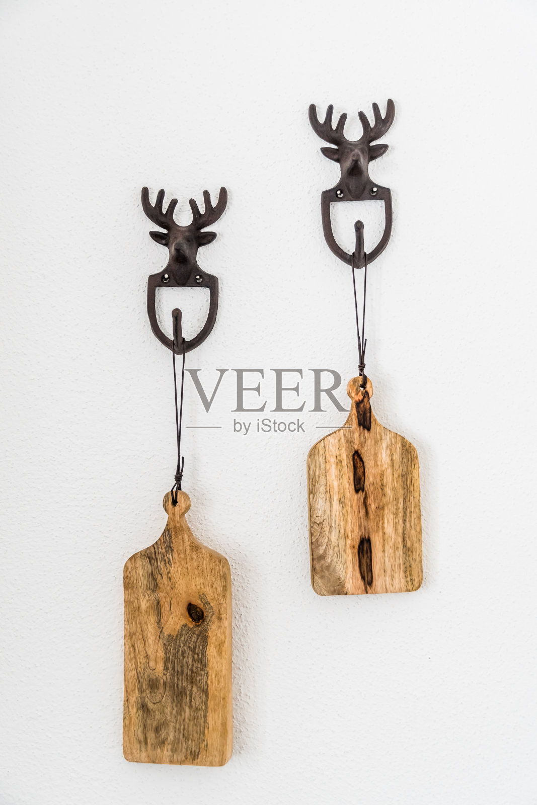 白色的墙上挂着装饰用的金属驼鹿钩,上面挂着厨房用的小木板,垂直的照片摄影图片
