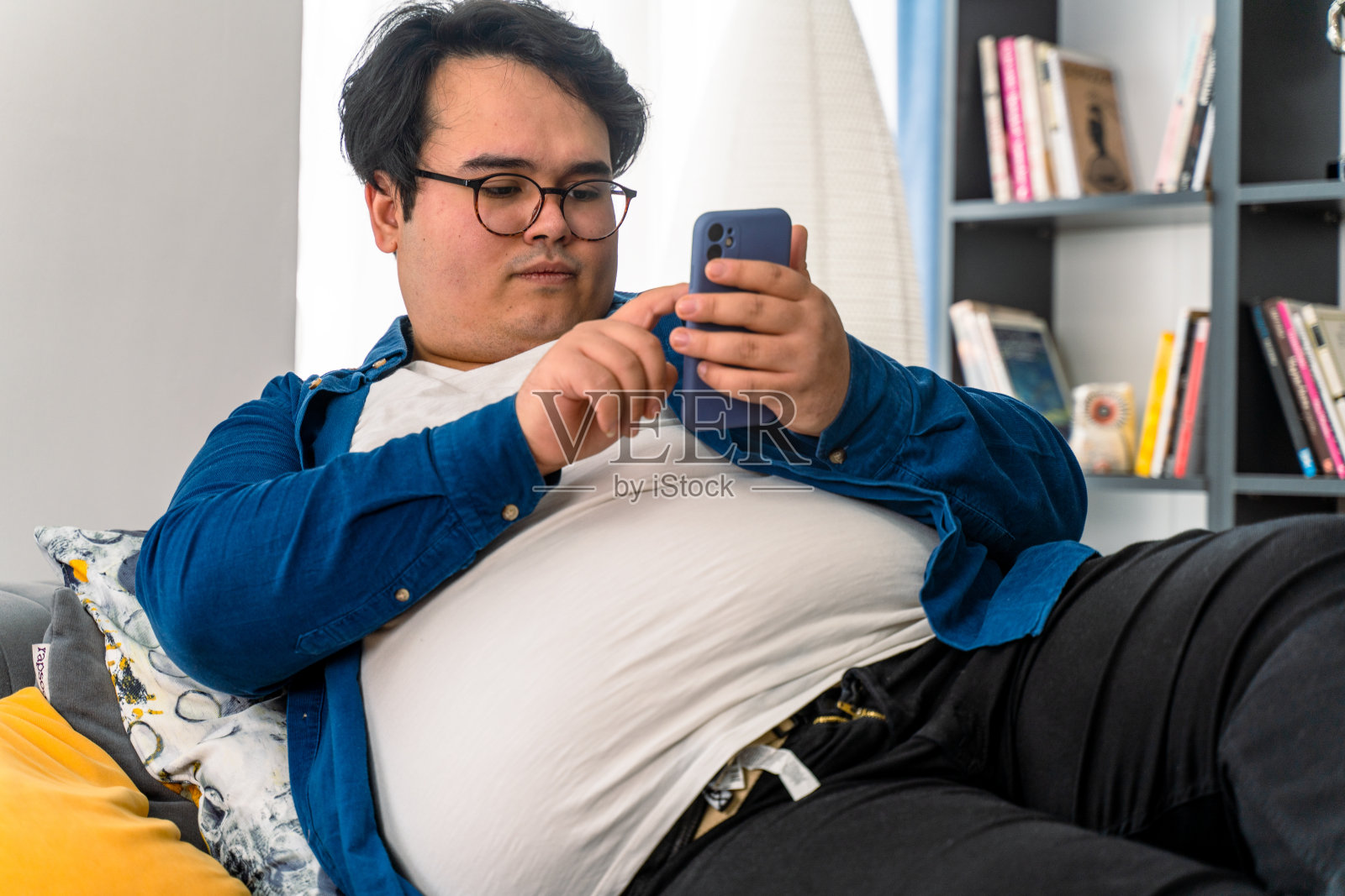 超重男孩躺在沙发上玩智能手机照片摄影图片