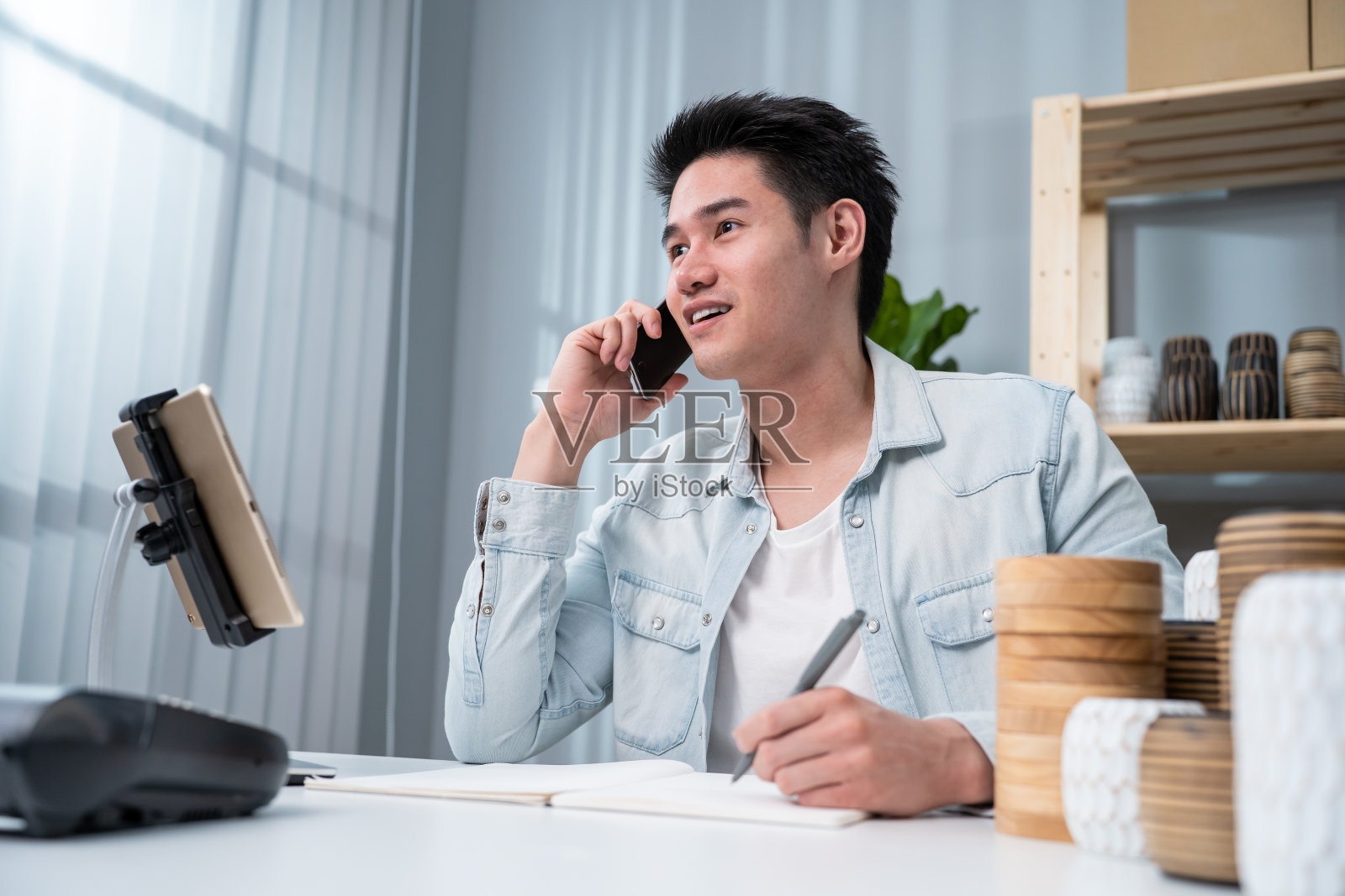 亚洲年轻人与客户通电话,查看花瓶货订单。有吸引力的商业男性工作准备包裹盒子,检查电子商务航运网上零售销售在家里的仓库商店。照片摄影图片