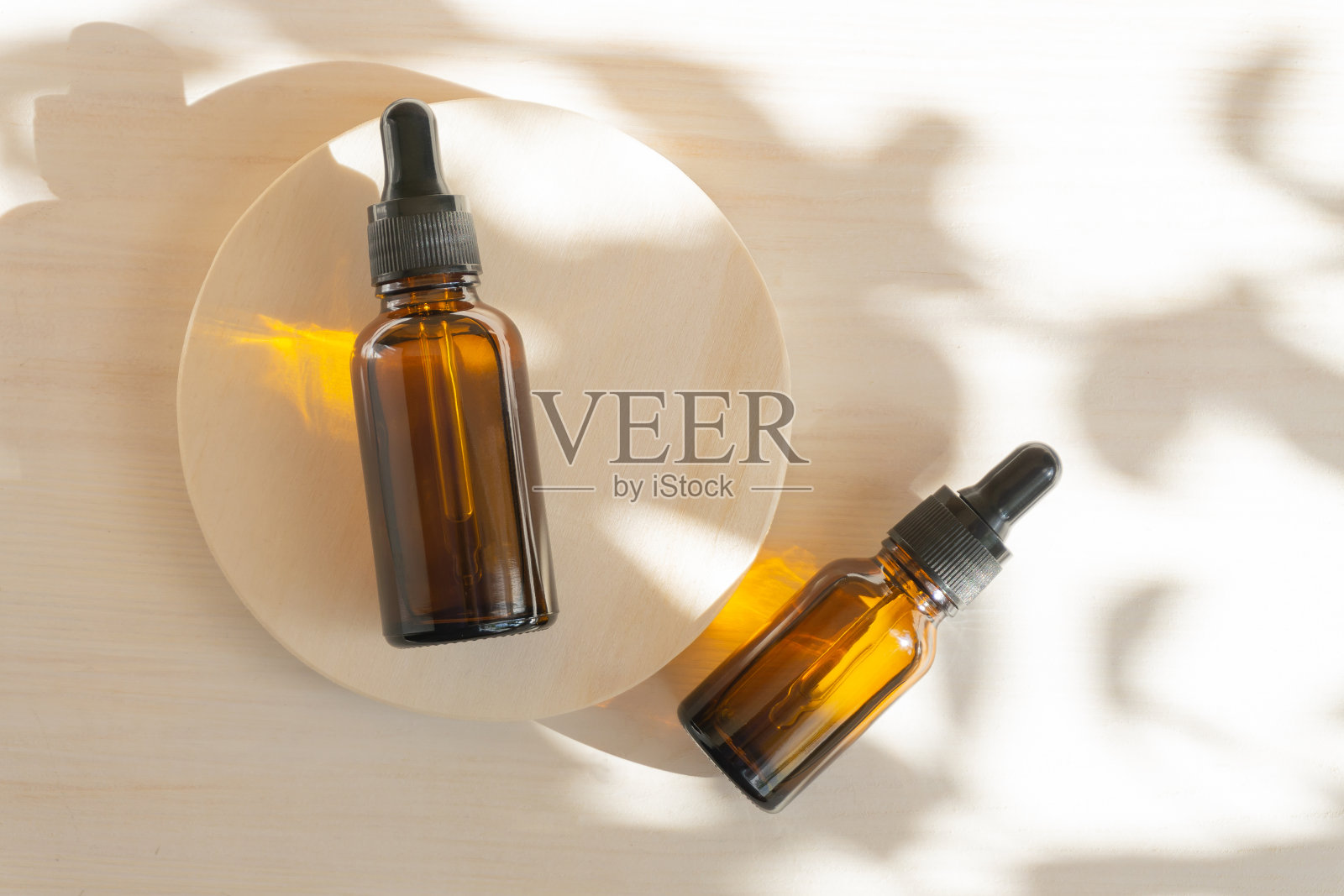 面部精华液,琥珀色玻璃瓶,圆形木架上有滴管盖。平躺,白色背景与花的阴影。化妆品展示的几何概念平台照片摄影图片
