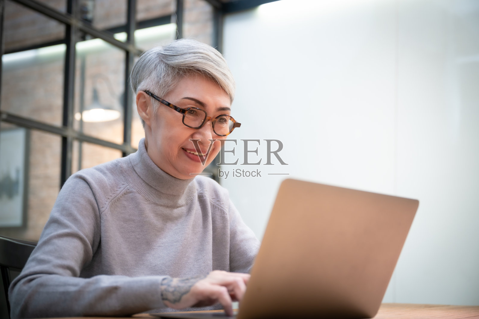 成熟的亚洲女商人戴着眼镜,使用笔记本电脑,坐在办公桌旁。快乐的老员工50多岁的女商人照片摄影图片