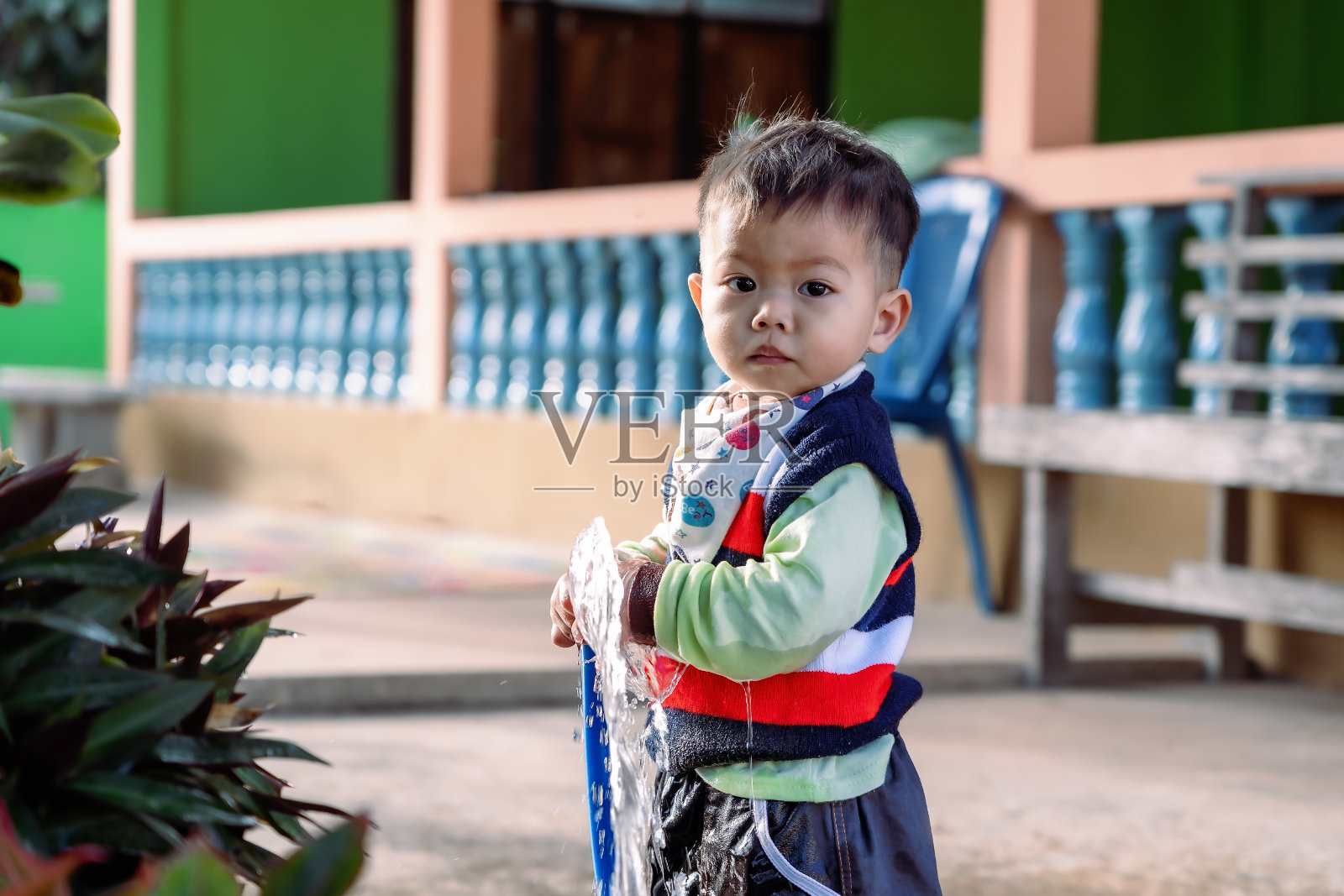 在阳光明媚的日子里,可爱的亚洲幼童在家里后院用花园软管浇花和草坪,玩得很开心。儿童小帮手学习户外园艺。童年的概念照片摄影图片