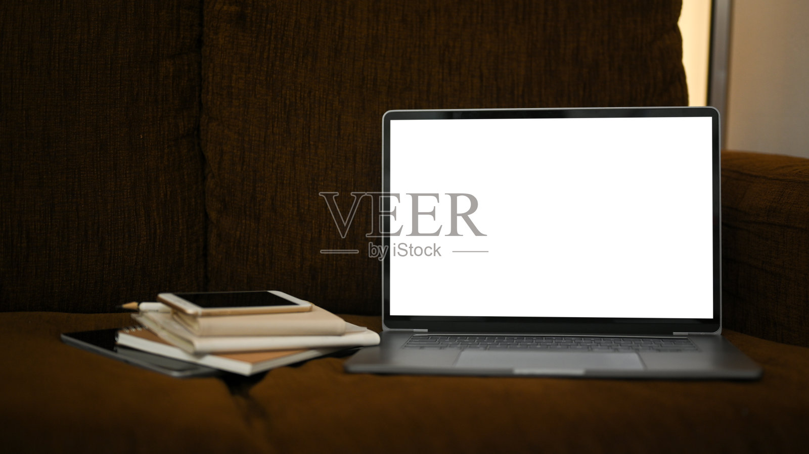 笔记本电脑和书在舒适的棕色沙发上。照片摄影图片