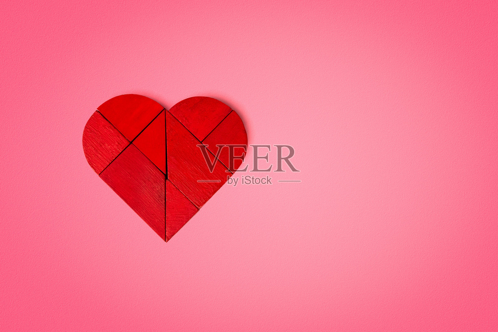 红心形状的木制拼图在红色(粉红色)纸纹理背景与vignette在边缘和复制空间的右边。爱情和情人节的概念。照片摄影图片