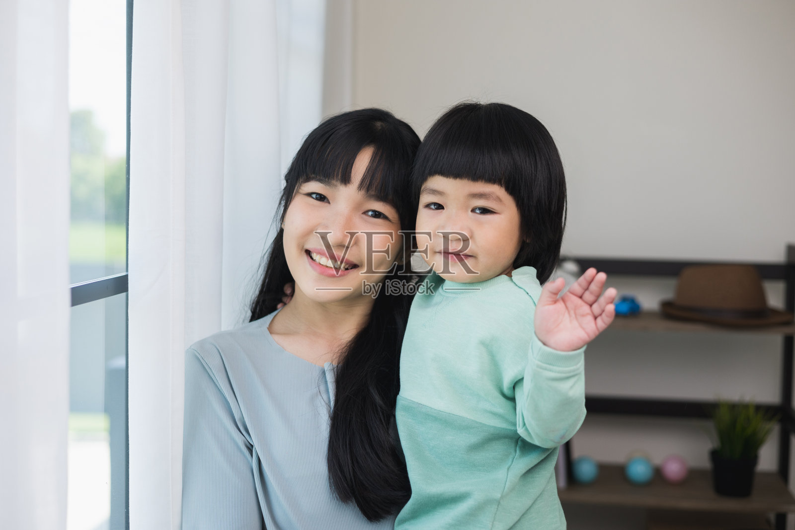 妈妈抱着儿子看着镜头在屋子里感到高兴。母亲抱着小男孩在客厅里走来走去,对着镜头微笑。照片摄影图片