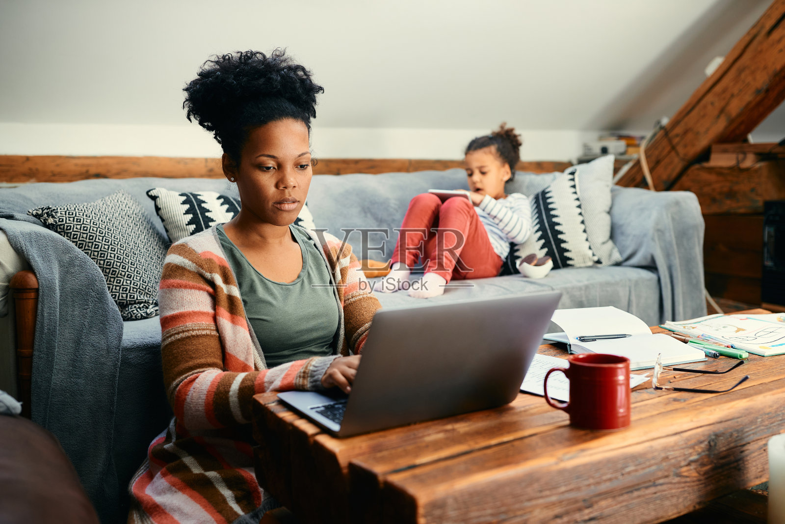 非洲裔美国人呆在家里,当她的女儿在沙发上放松的时候,她的母亲在笔记本电脑上工作。照片摄影图片