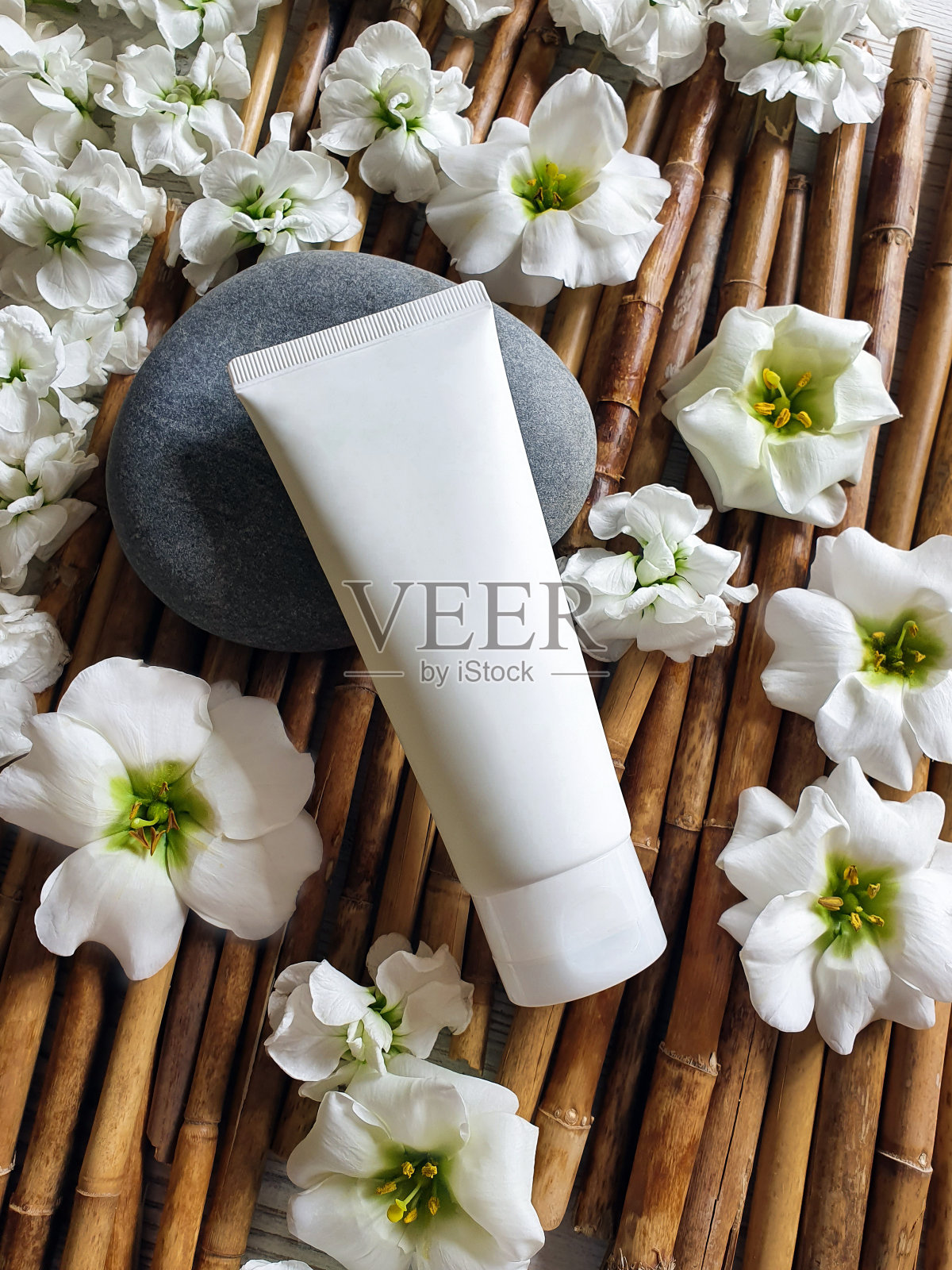 模拟白色塑料瓶管与白色的花朵和石头在竹子的背景。天然有机化妆品概念。生活方式,平照片摄影图片