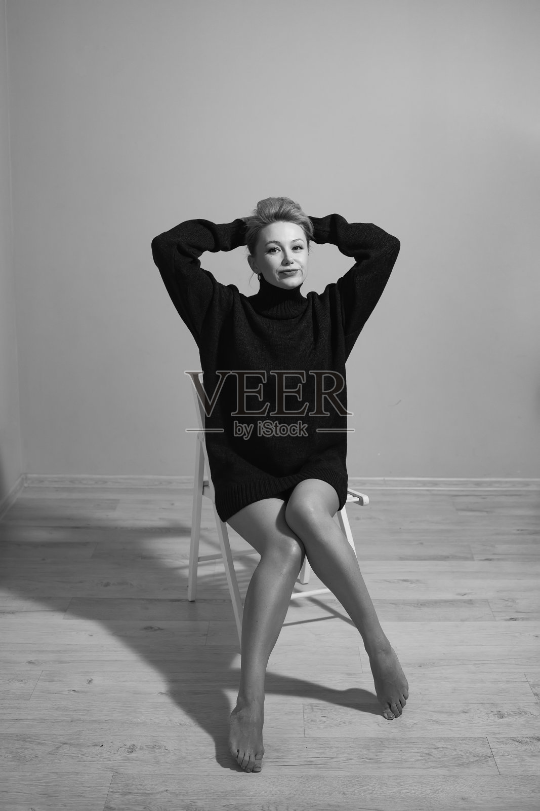 一名时尚的年轻女子,穿着舒适的黑色毛衣,坐在工作室的椅子上照片摄影图片