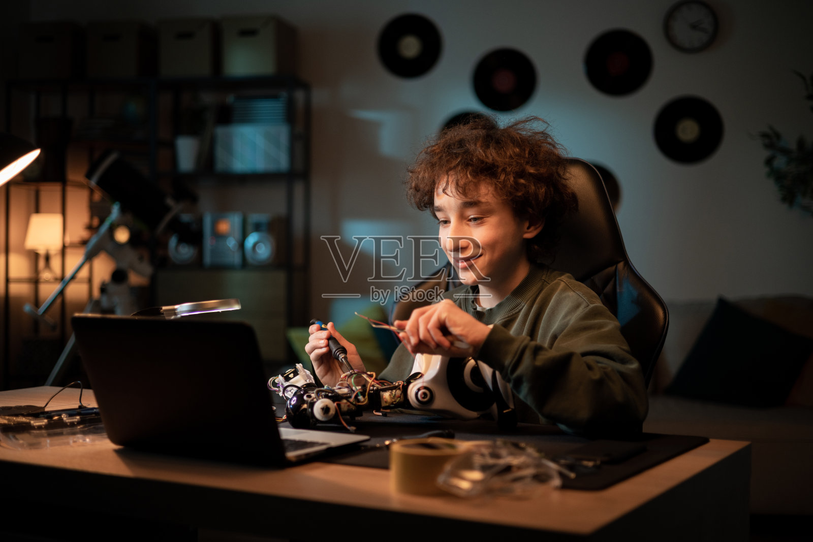 男孩通过笔记本电脑上的网络摄像头和朋友聊天,展示他是如何学习焊接电子产品的,吹嘘机器人项目,解释玩具遥控的线缆连接照片摄影图片