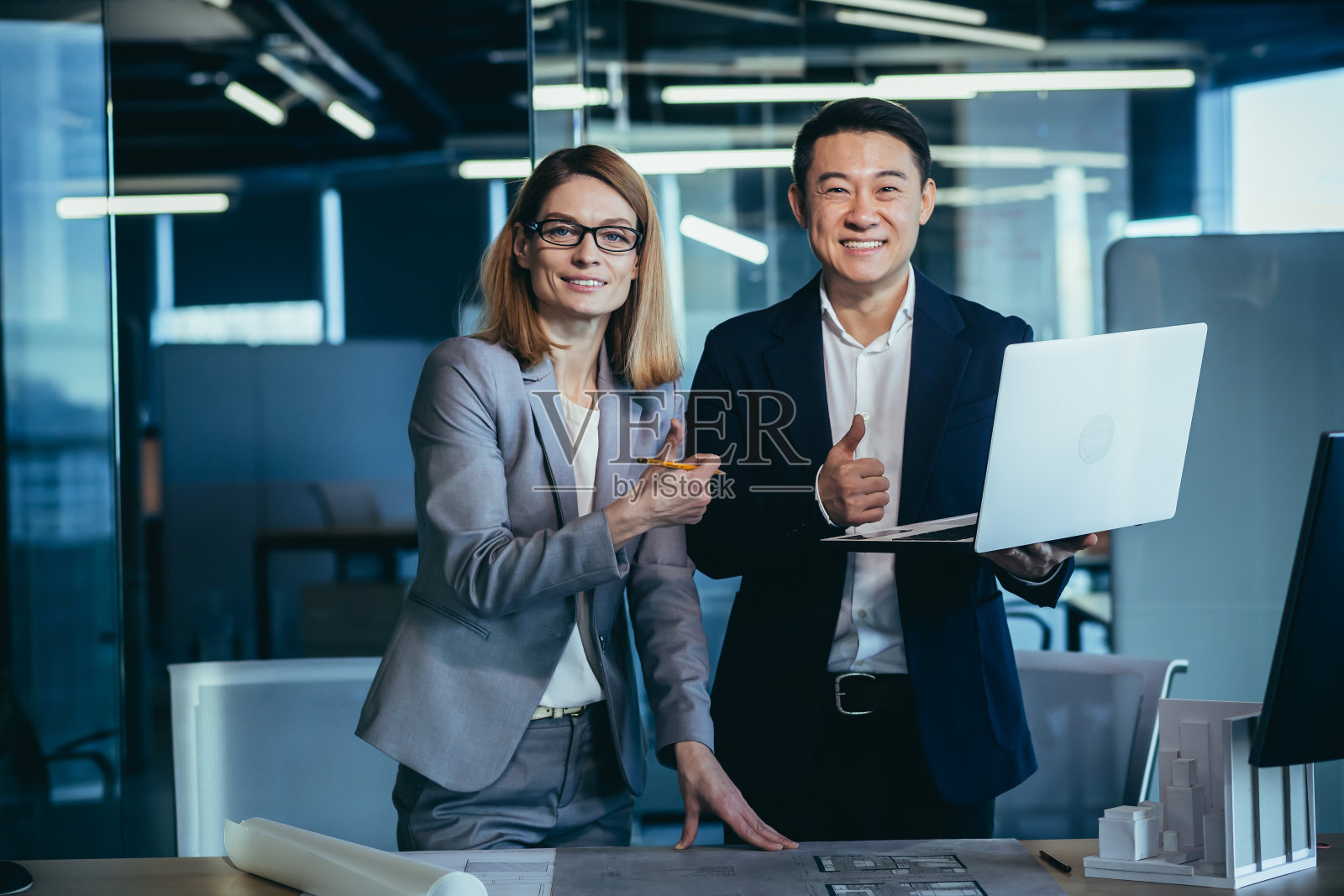 两个建筑师团队,看着摄像机,欣喜地微笑着完成的项目,保持拇指肯定照片摄影图片