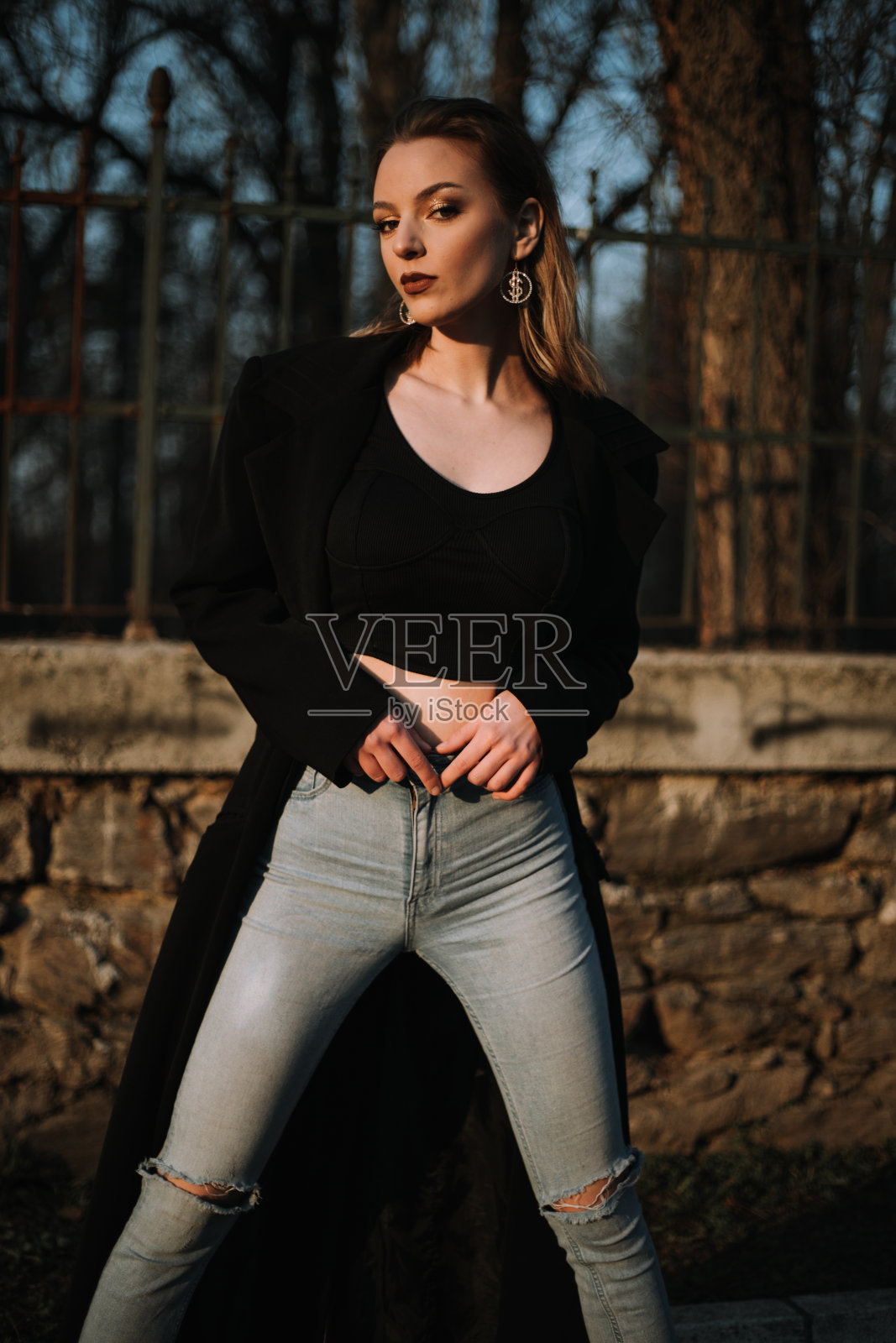 穿着黑色外套的漂亮年轻女子摆出姿势,手臂放在腰带上照片摄影图片