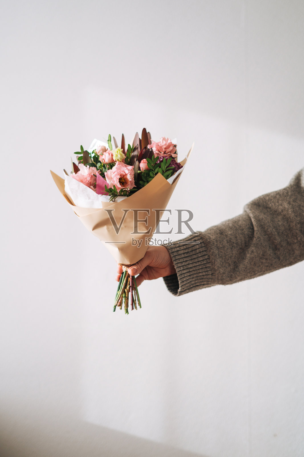 年轻女子身穿灰色针织毛衣,手里拿着花束,背景是灰色的照片摄影图片