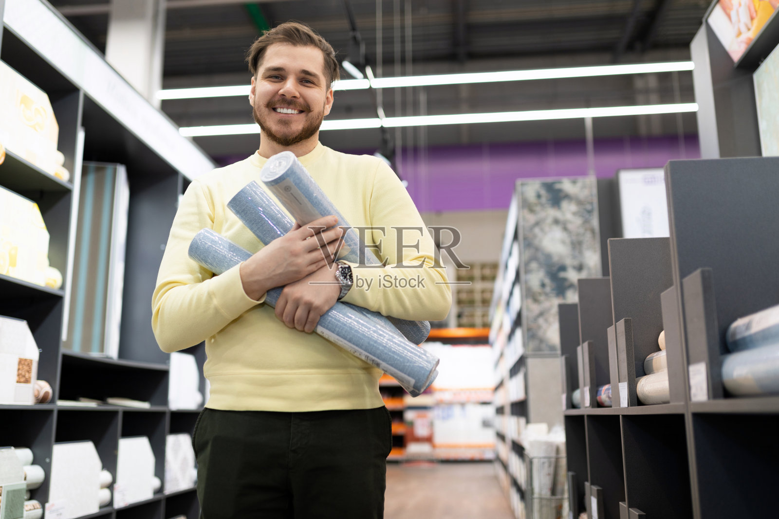 在一家五金店里,一位开心的顾客手里拿着一卷一卷的无纺布壁纸,面带微笑地看着镜头照片摄影图片