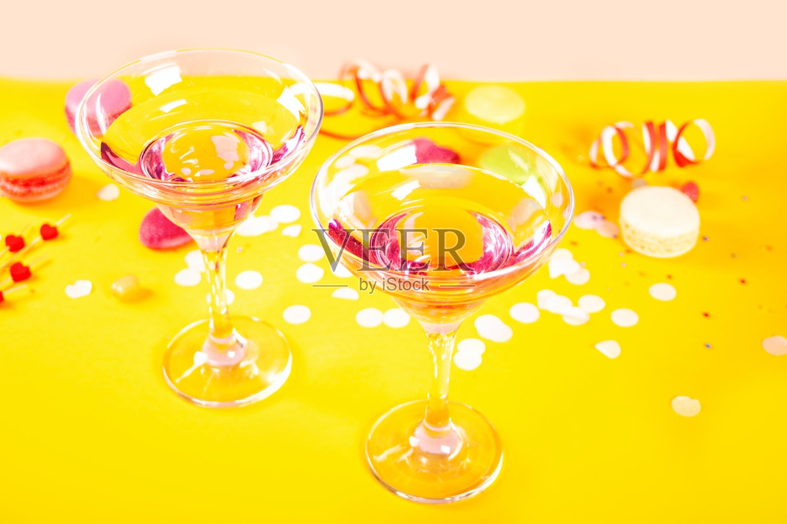 粉红色鸡尾酒杯,黄色背景上的心形糖果。生日派对或情人节的概念。照片摄影图片