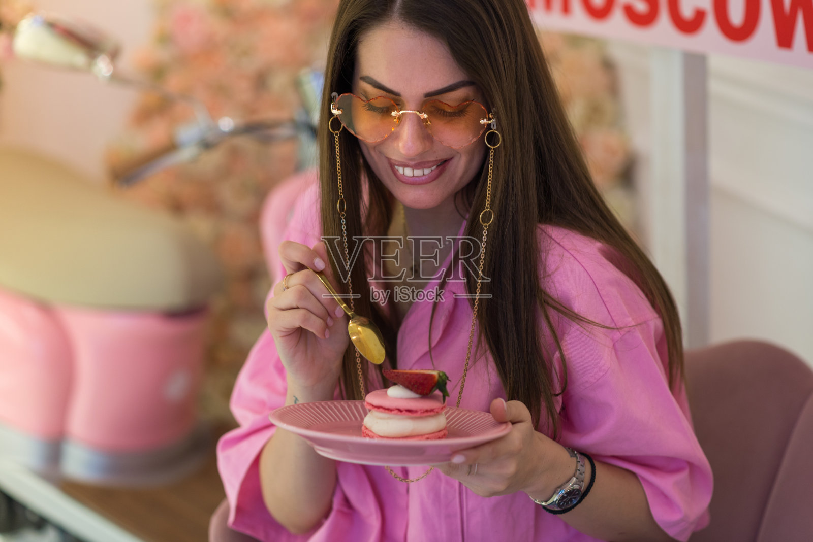 穿着粉色衬衫的漂亮女人吃着美味甜美的粉色蛋白杏仁饼,库存照片照片摄影图片