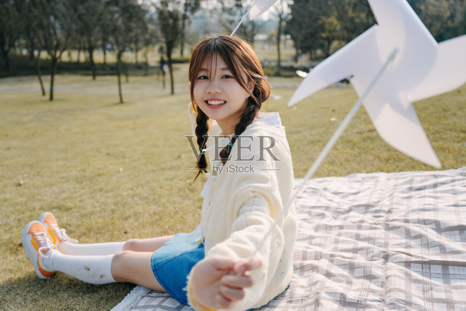 一个美丽的亚洲女孩坐在毯子上在一个阳光明媚的日子玩纸风车照片摄影图片