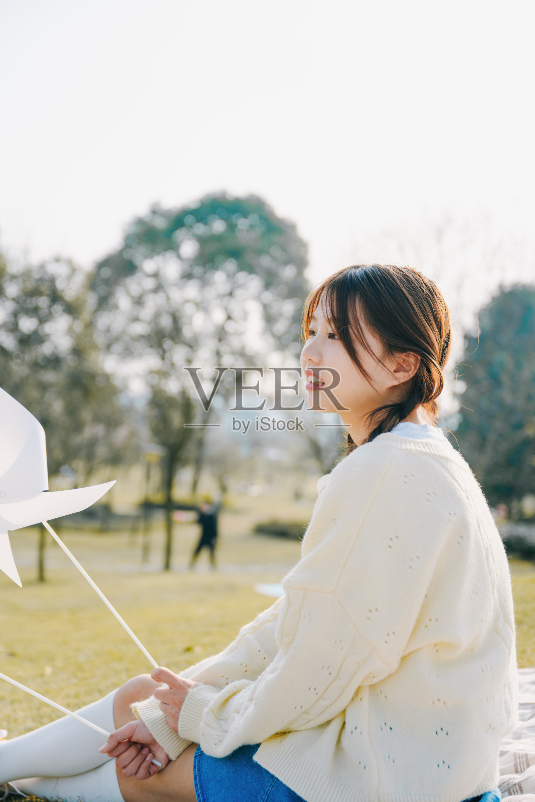 一个美丽的亚洲女孩坐在毯子上在一个阳光明媚的日子玩纸风车照片摄影图片