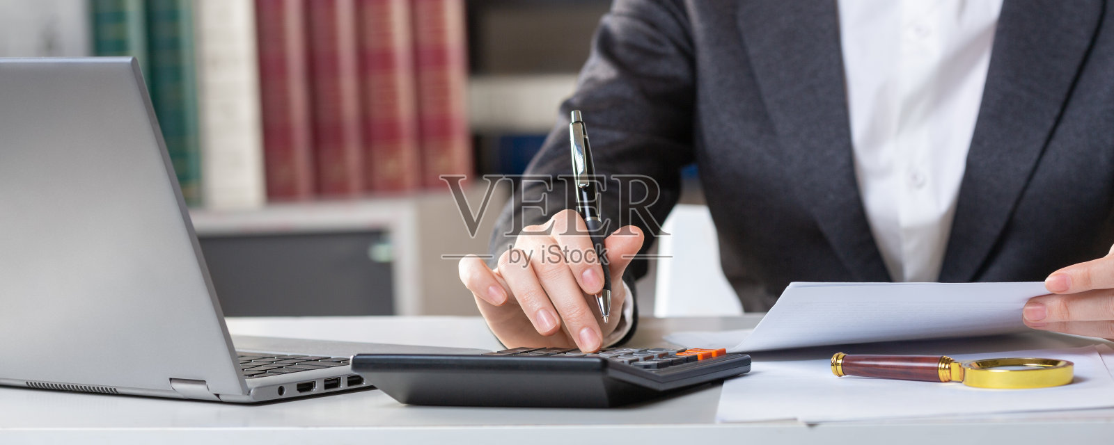 在办公室里,穿着西装的女性手在工作场所使用手动计算器,特写镜头,选择性聚焦。照片摄影图片