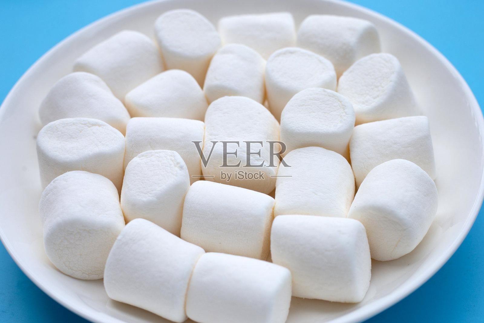 白色棉花糖在蓝色背景的盘子上。照片摄影图片
