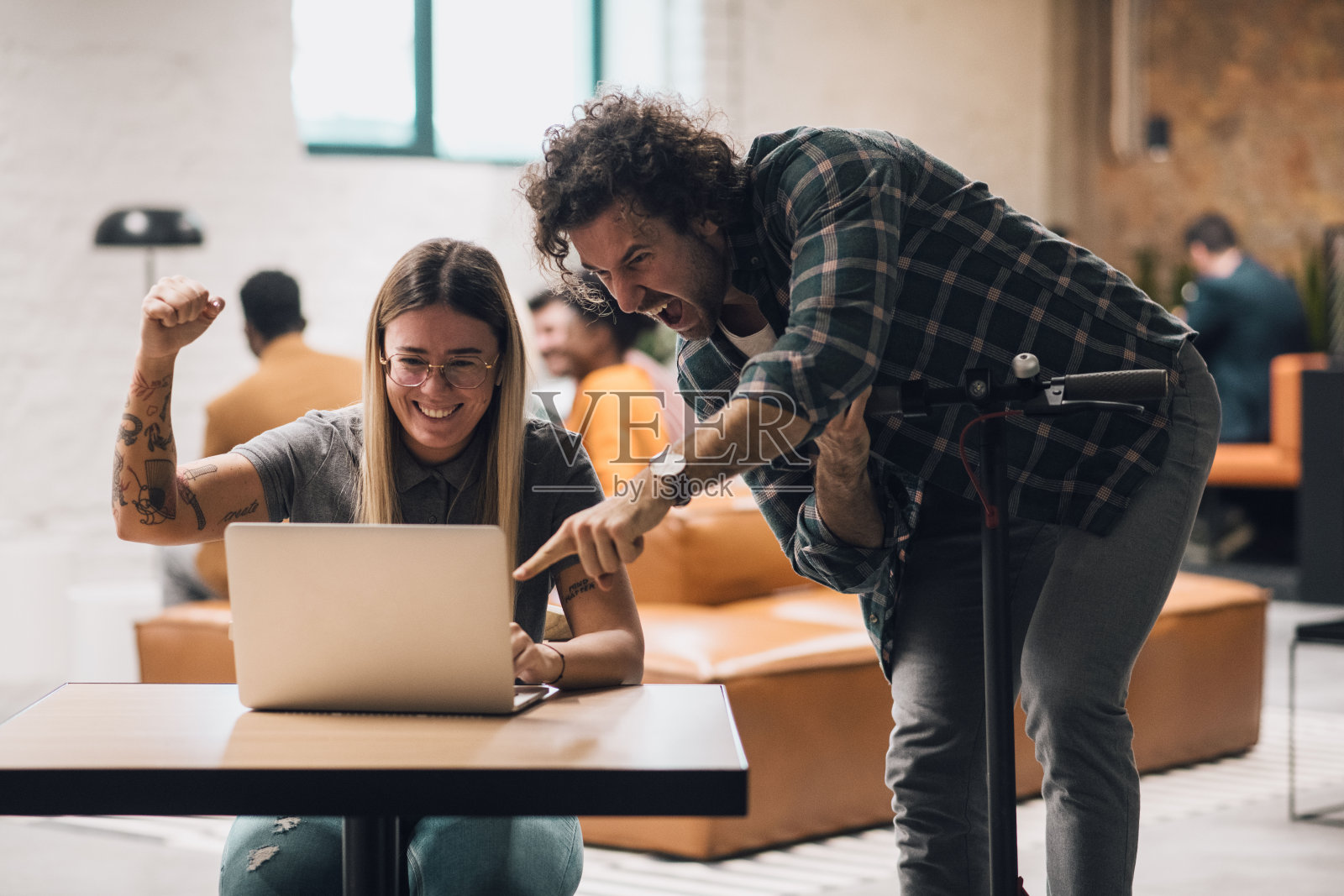 在现代的办公室里,老板和他的员工一边对着笔记本电脑微笑,一边庆祝成功。照片摄影图片