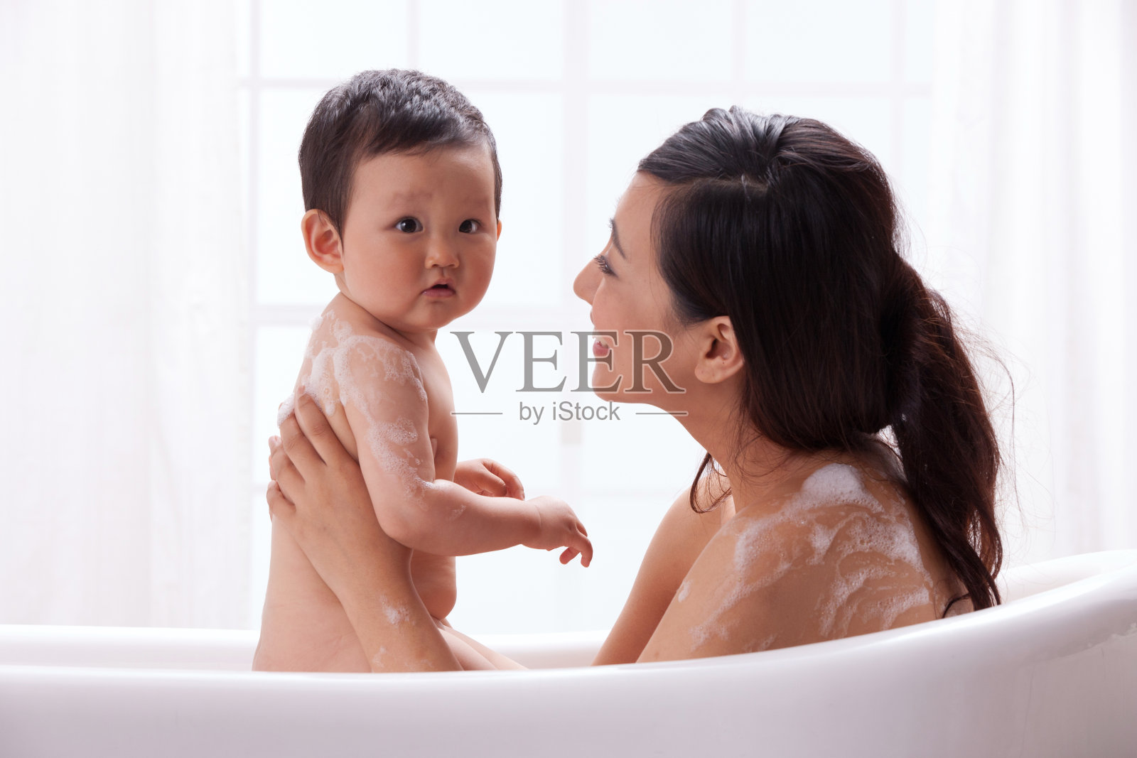 母亲和婴儿坐在浴缸中洗澡照片摄影图片