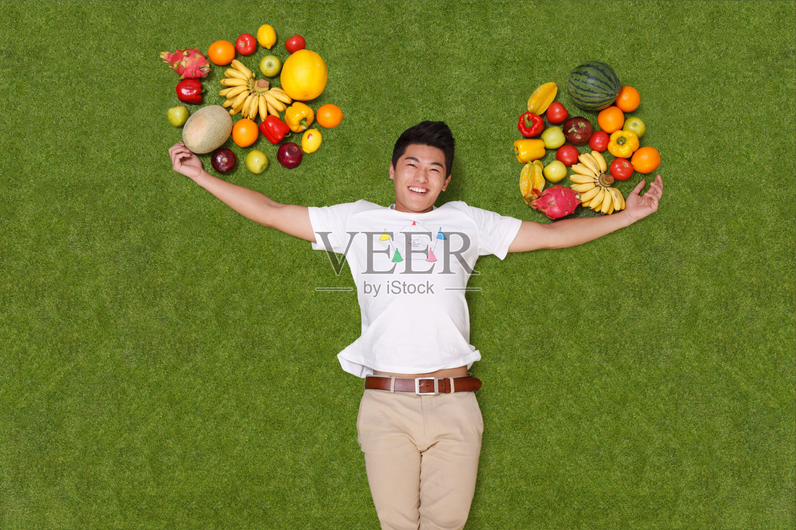 年轻男子躺在草地上手托着水果照片摄影图片